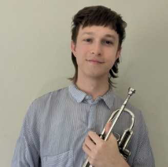 A young man with dark hair, wearing a blue and white striped button-up shirt, holding a silver trumpet, standing against a plain light-colored wall.