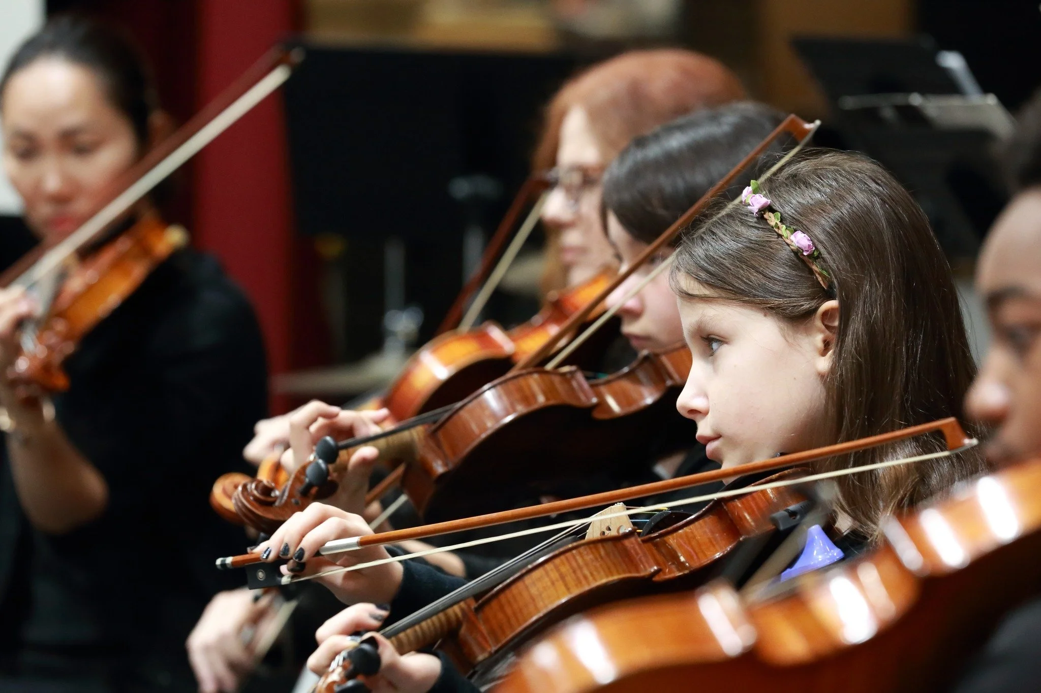 Orchestra performing on stage with a conductor, featuring a female cellist in the foreground.