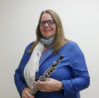 Woman in blue shirt holding an oboe with a white scarf around her neck, standing against a white background.