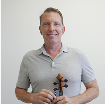 A man smiling and holding a violin against a plain light-colored background.