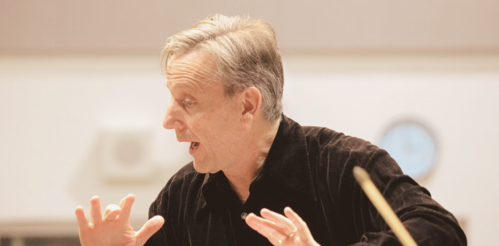 An elderly man with gray hair, wearing a black shirt, appears to be speaking passionately with animated hand gestures.