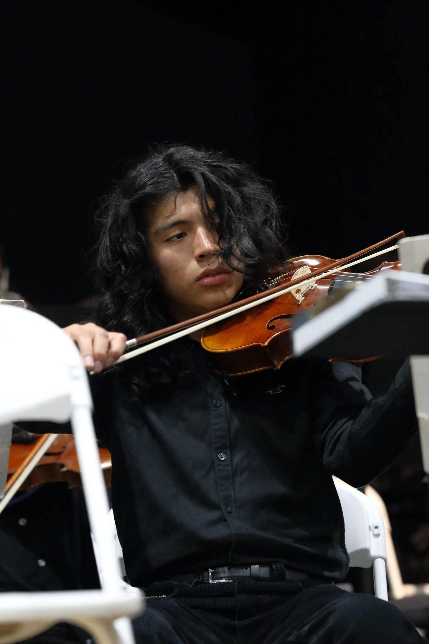 A close-up photo of a young man playing viola against a black background