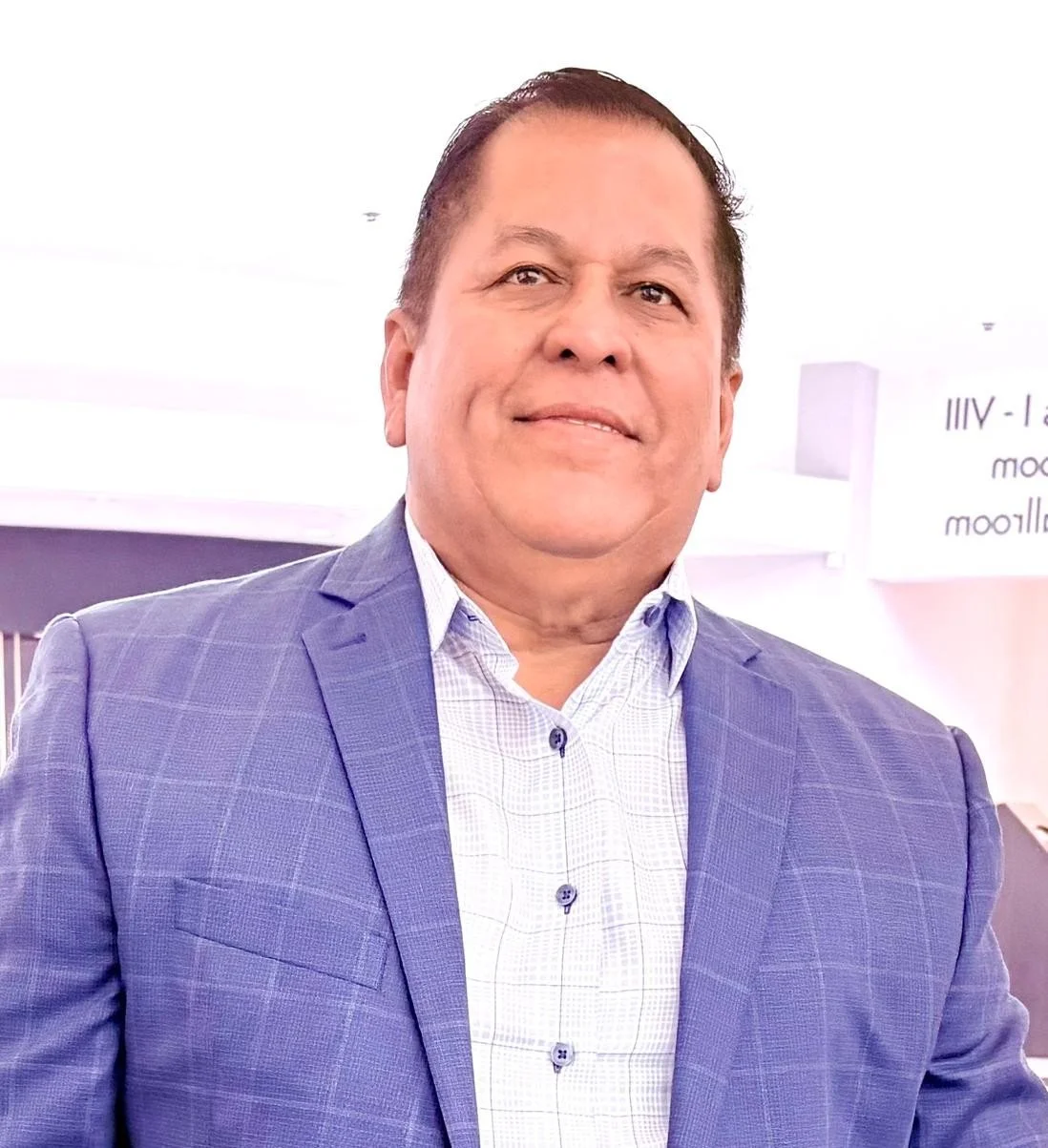 Portrait of a middle-aged man in a blue checkered suit and white dress shirt, smiling at an indoor event.