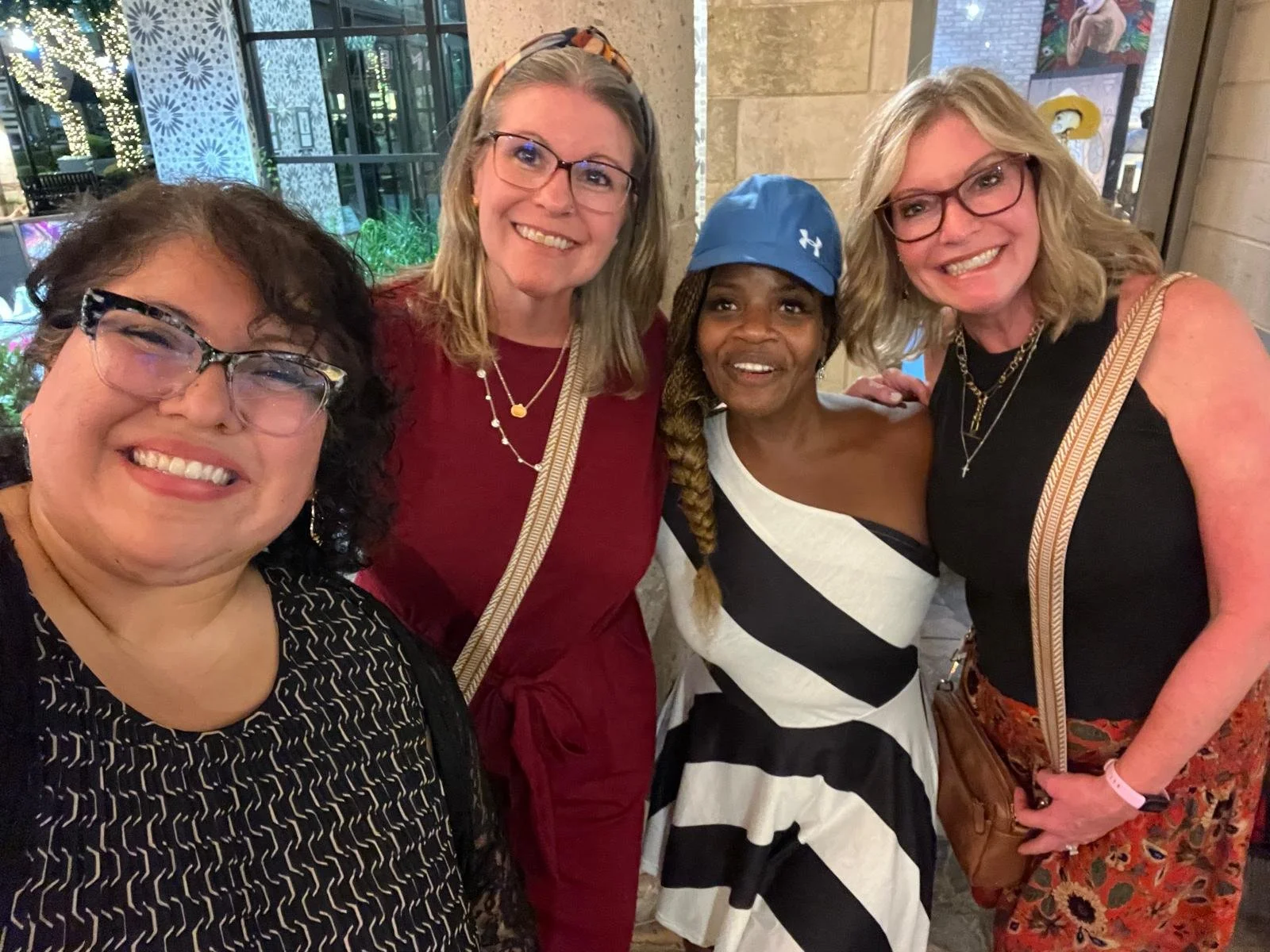 Group of five women smiling and posing for a photo indoors, with festive holiday decorations visible in the background.