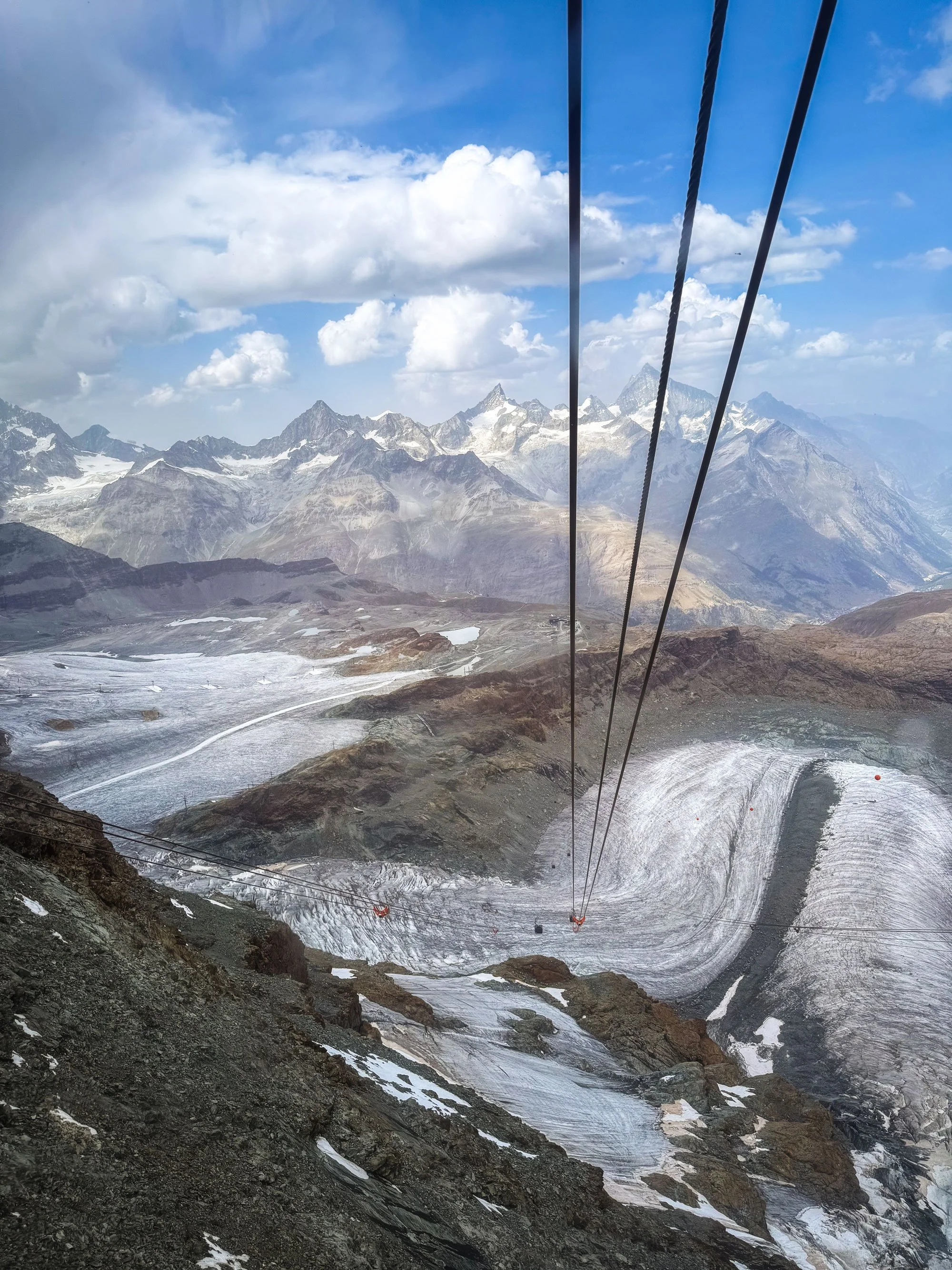 Mountain landscape with snow-capped peaks, a glacier, and a cable car system in the foreground.