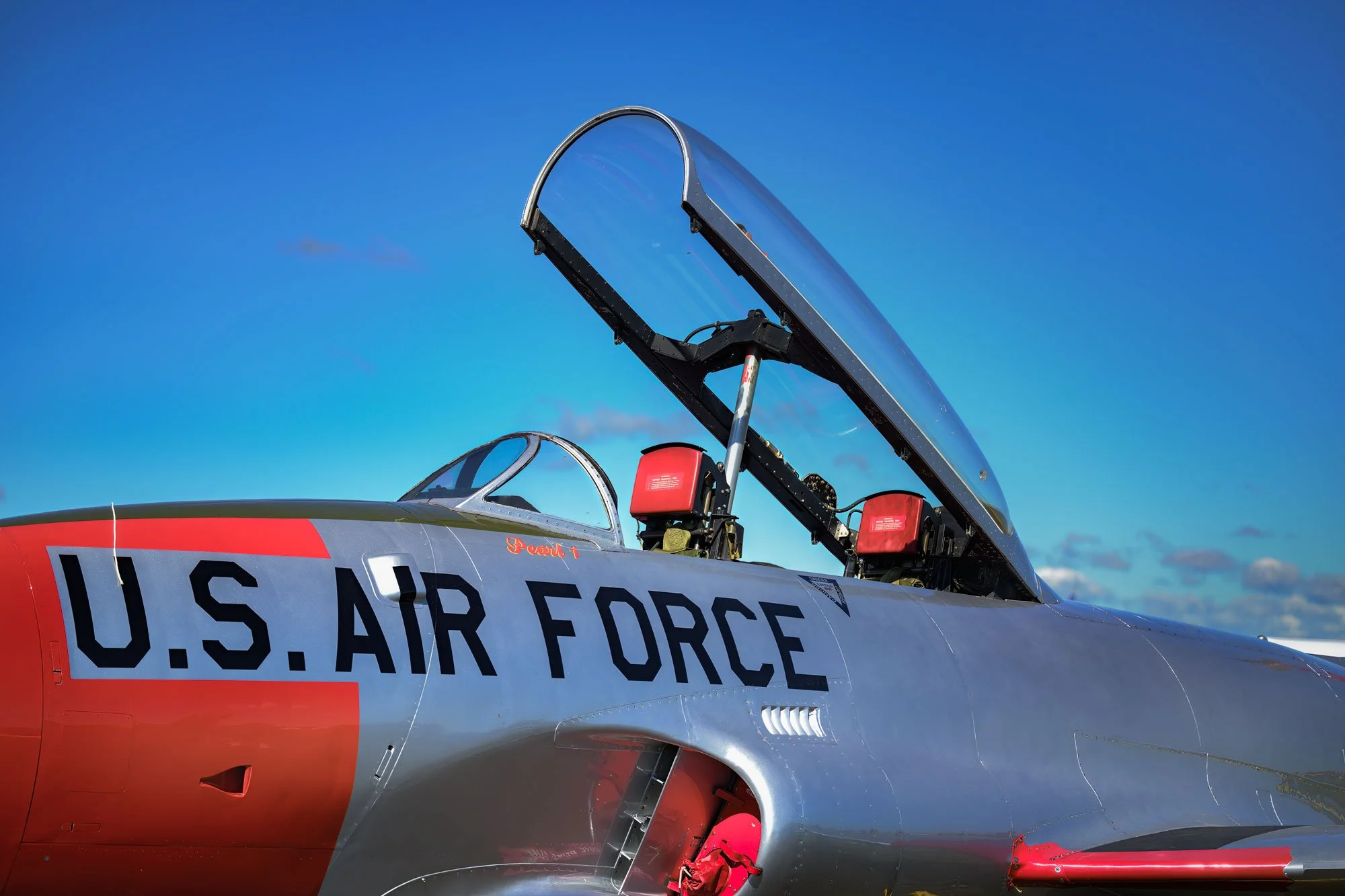 Close-up of a U.S. Air Force fighter jet cockpit with the canopy open against a blue sky.