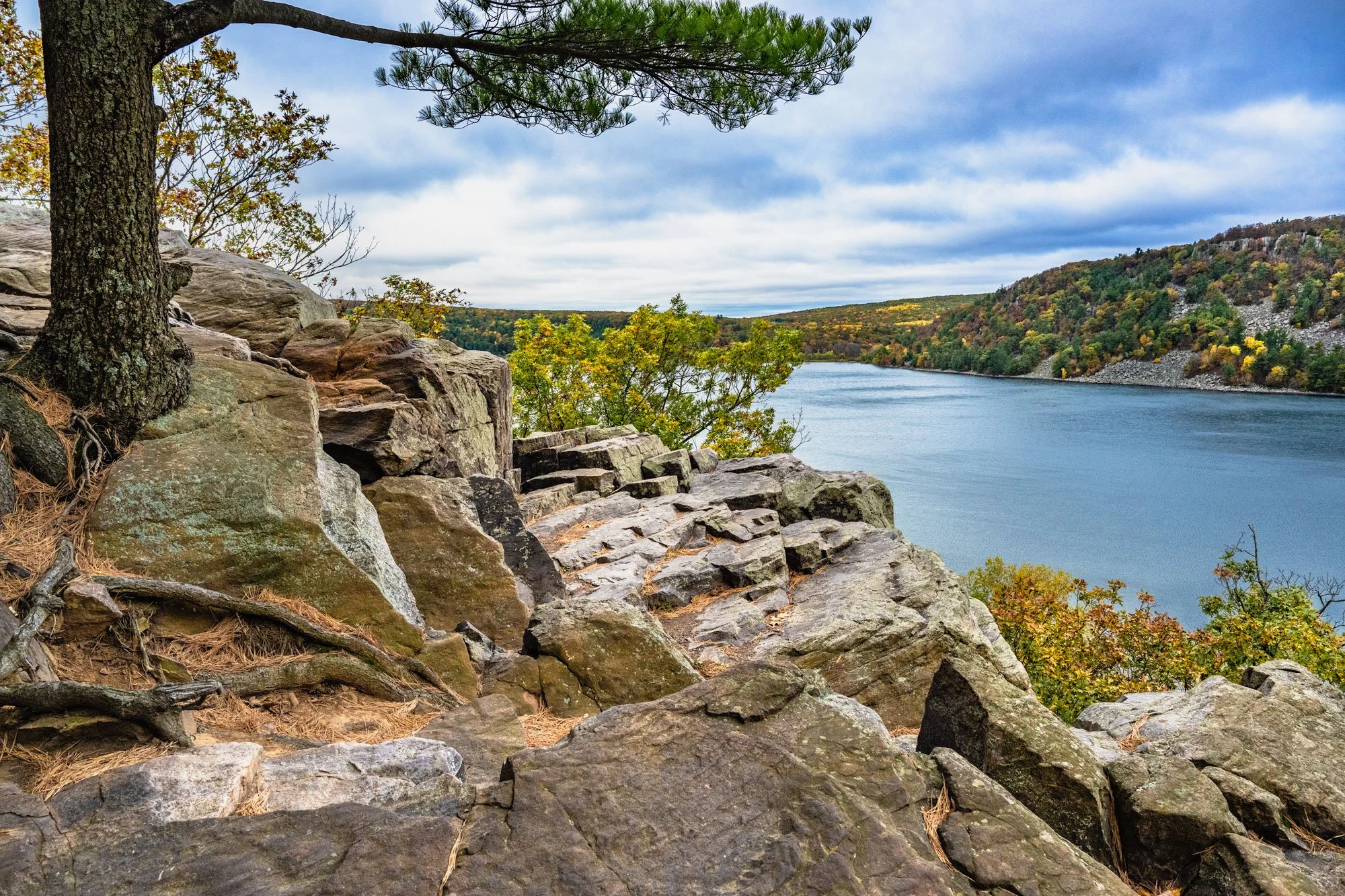Rocky cliff overlooking a river with autumn foliage and trees, cloudy sky