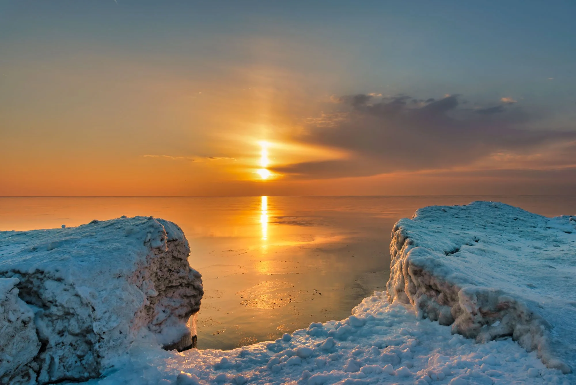 Sunrise over a frozen lake with ice formations in the foreground and clouds in the sky.