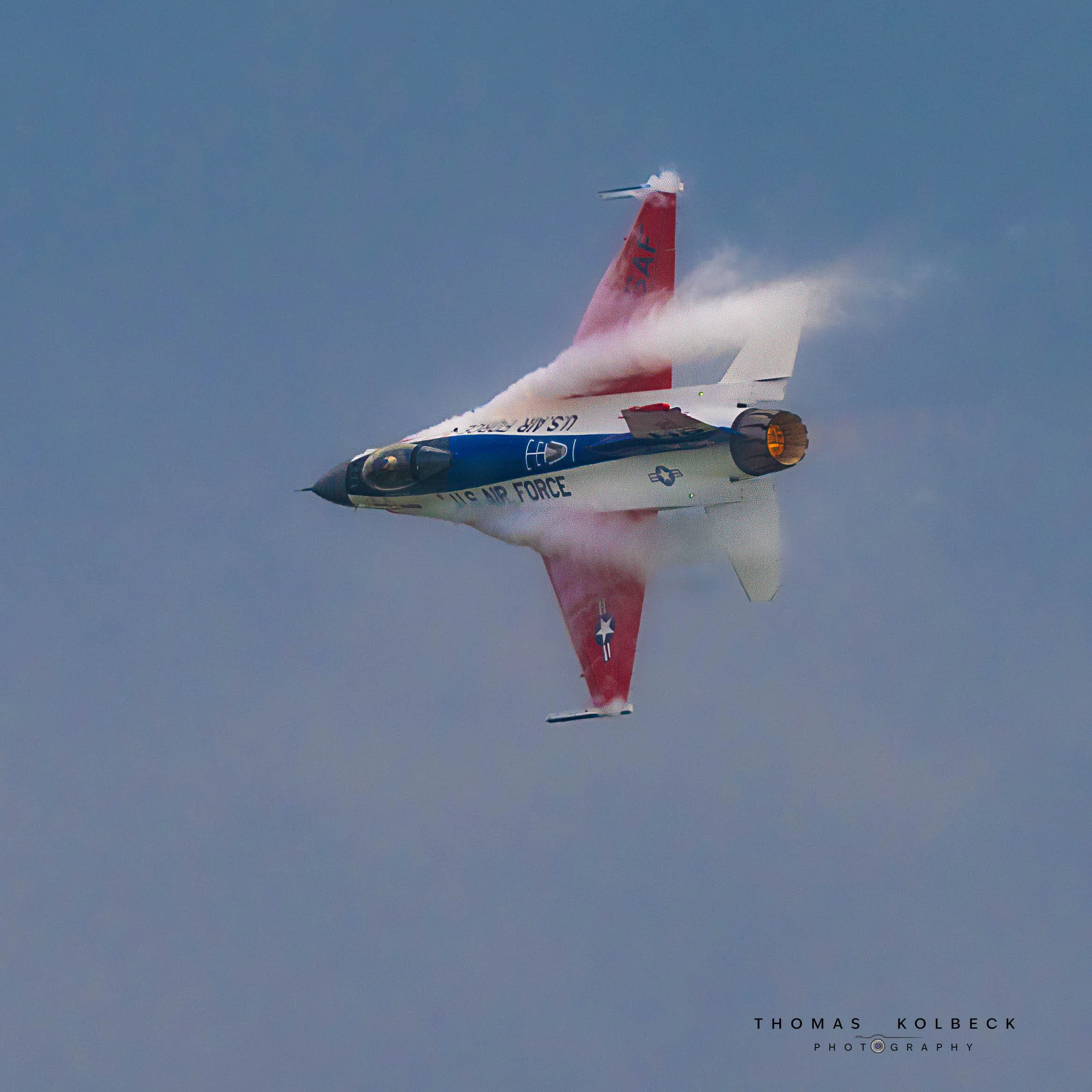 A jet aircraft performing an aerial stunt, leaving a trail of water vapor against a cloudy sky backdrop.