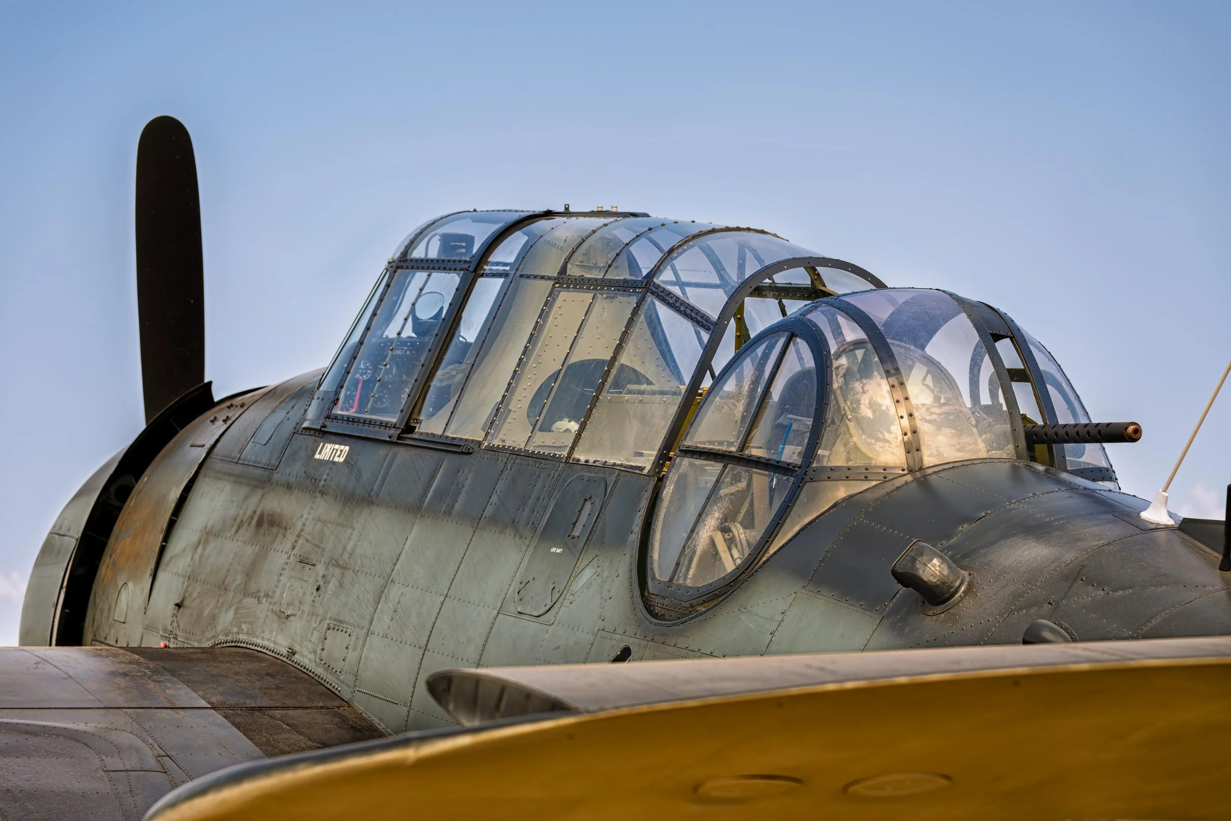 Close-up of the canopy and cockpit of a vintage military aircraft with a camouflage paint scheme, set against a clear sky.