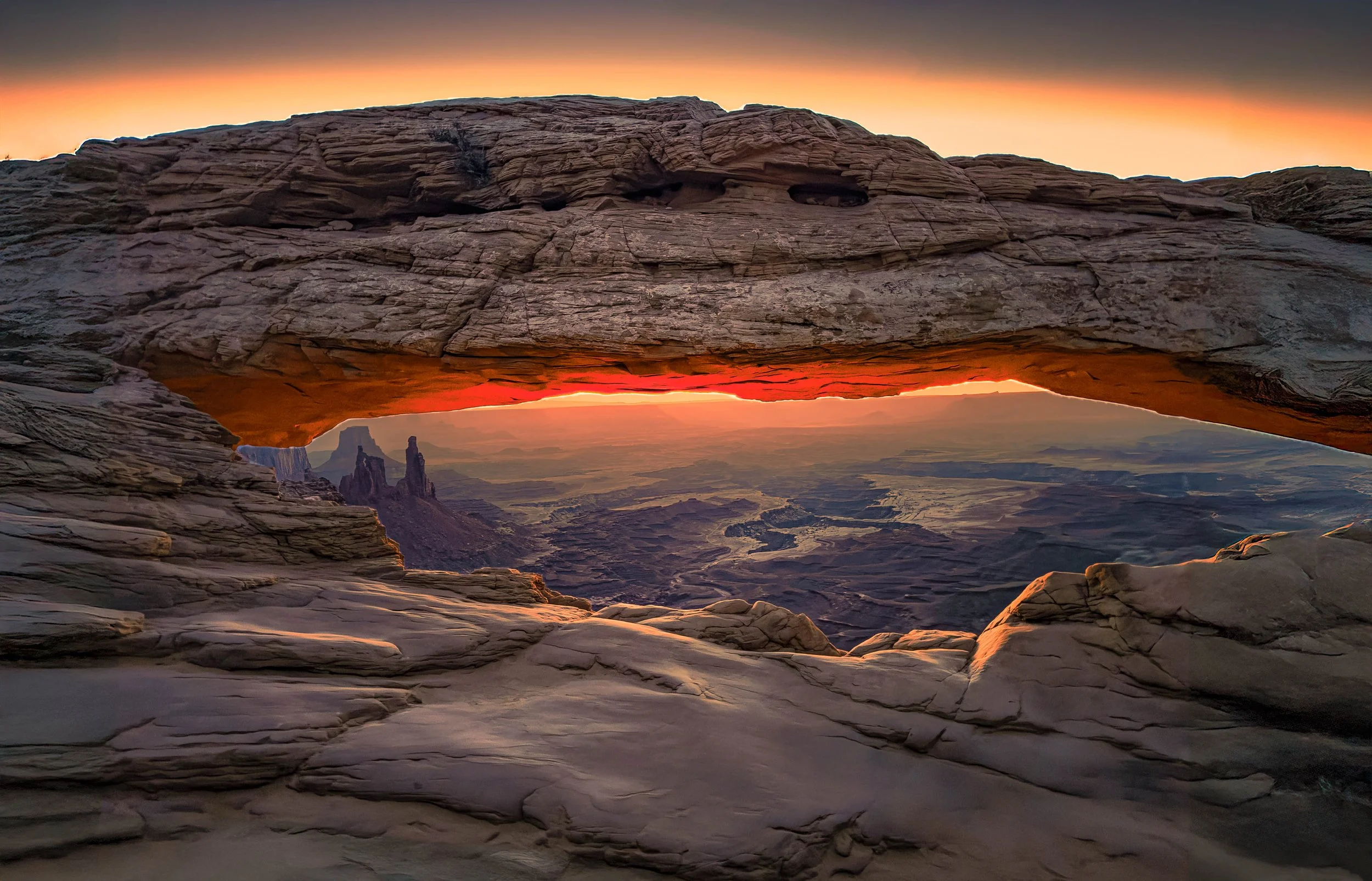 Sunset view through a natural rock arch with desert landscape and mesas in the distance.