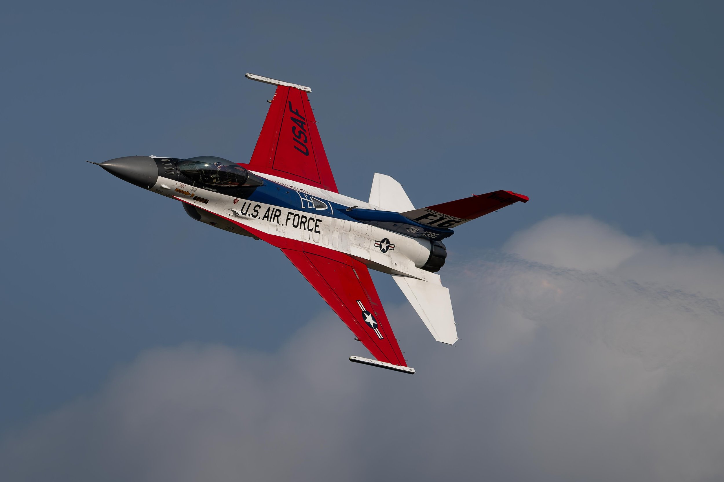 A U.S. Air Force fighter jet flying through the sky with a blue background and some clouds.