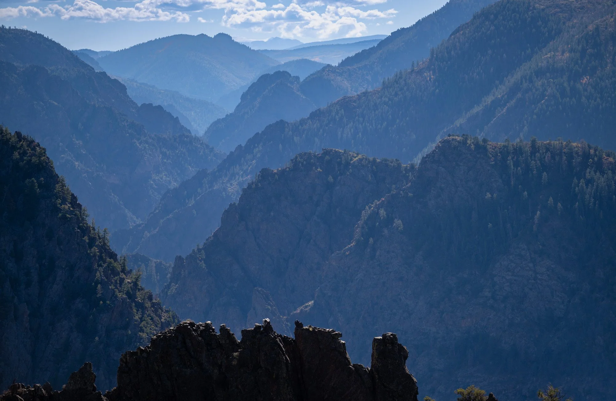 A scenic view of blue mountain ranges with peaks covered in green trees and a partly cloudy sky.