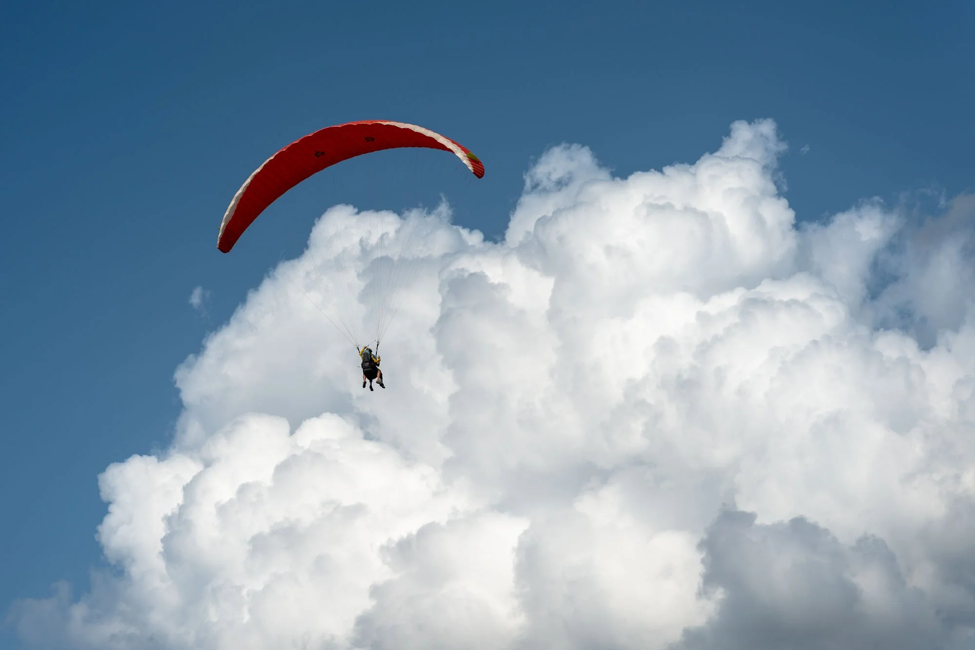 A person paragliding with a red and white canopy in the sky, flying among white clouds.