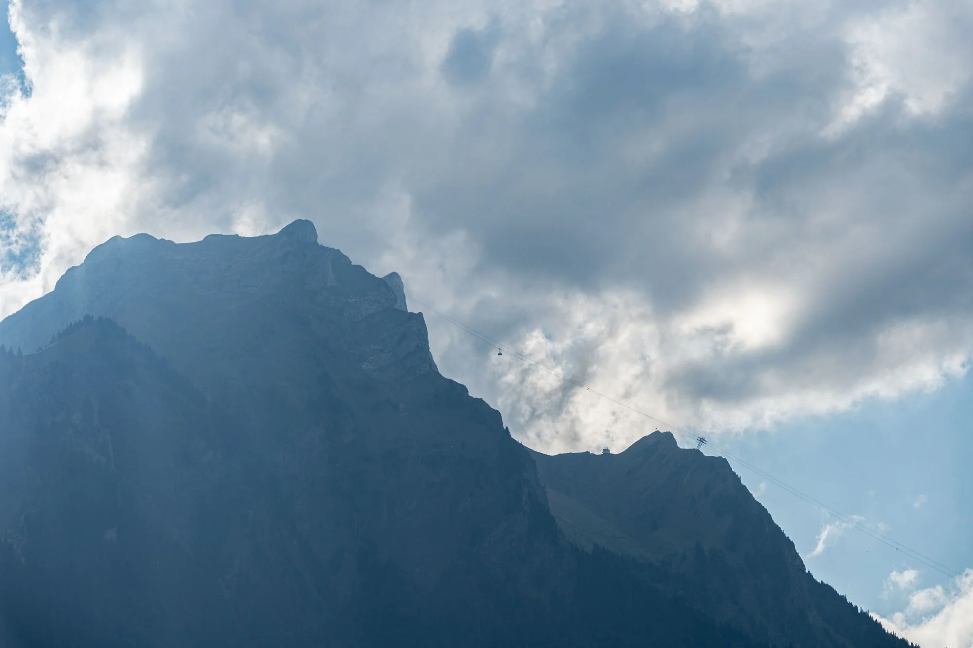 Mountain with cable car cable running across the sky with clouds