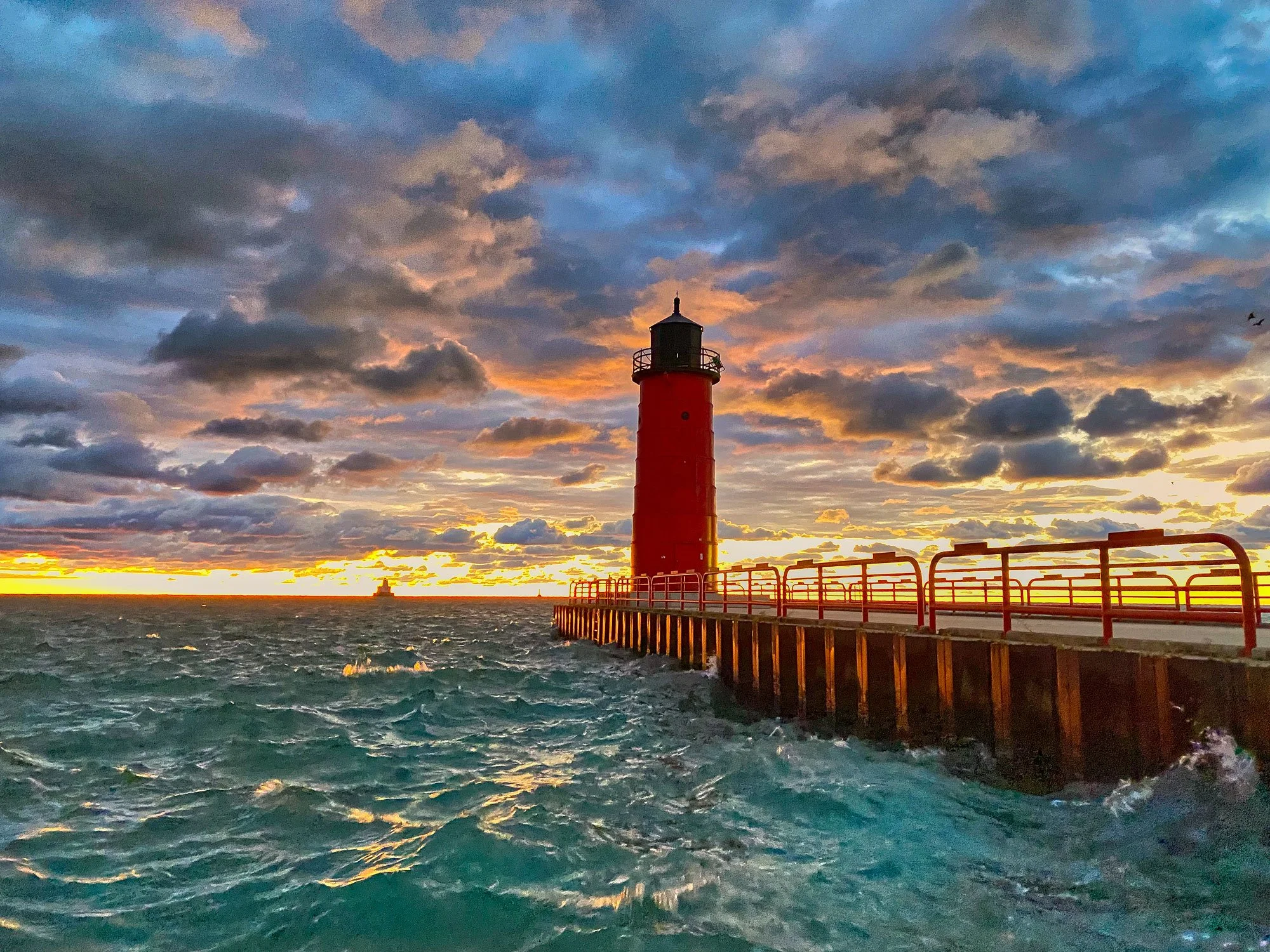 A lighthouse on a pier at sunset with a cloudy sky and choppy water.