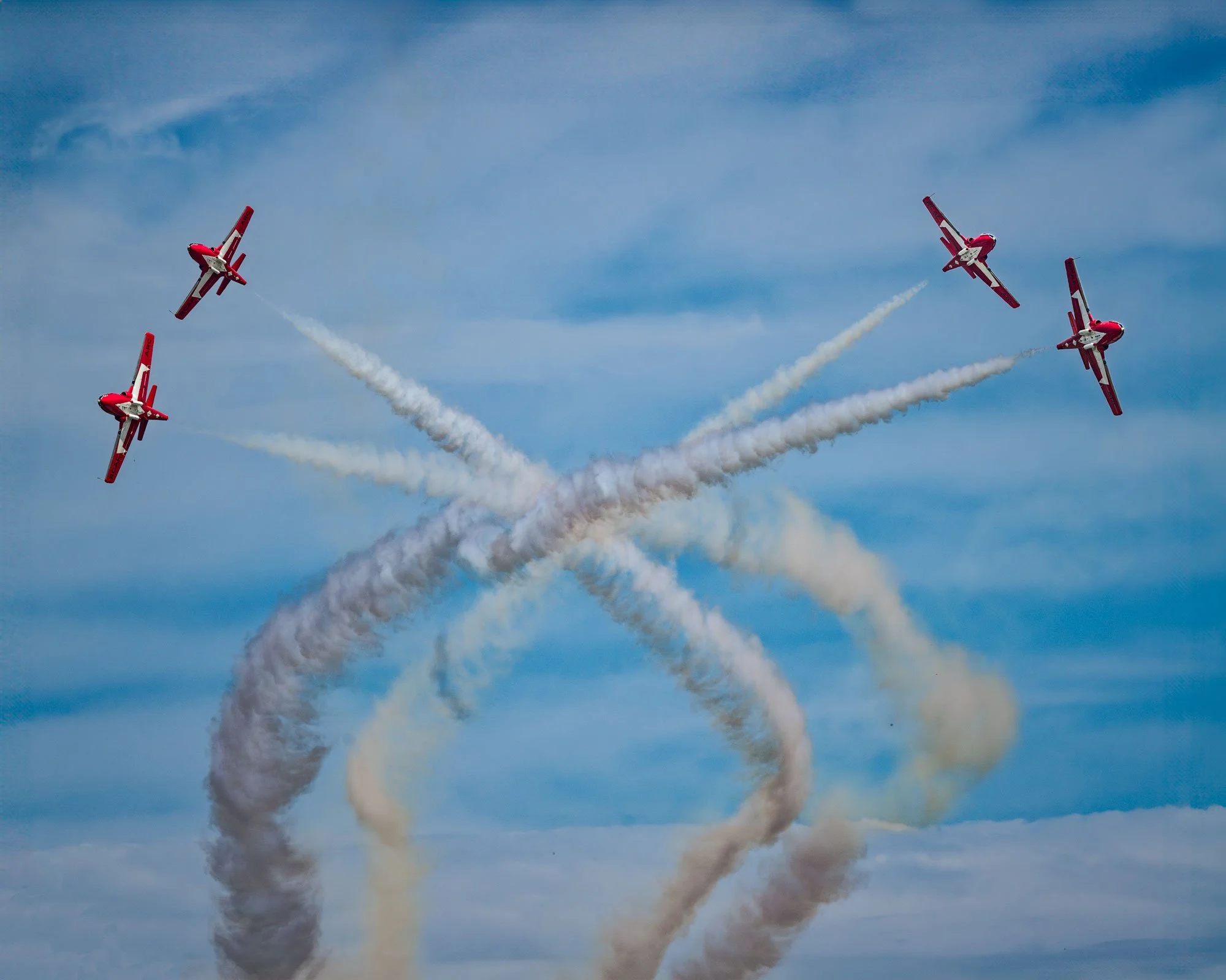Four red airplanes performing an aerial stunt and creating smoke trails in the sky.