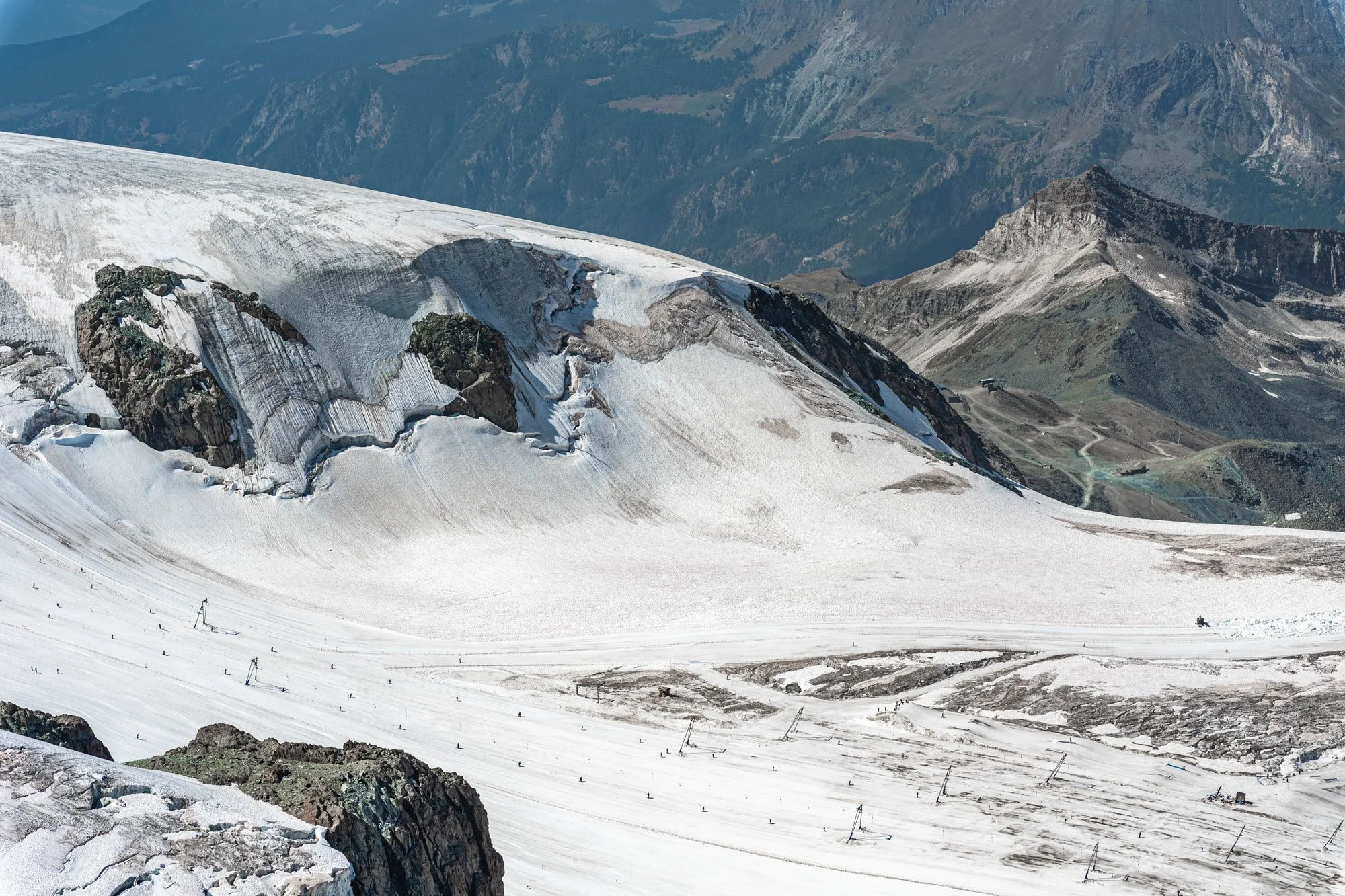 Snow-covered mountain landscape with rocky peaks, patches of ice, and ski lift infrastructure