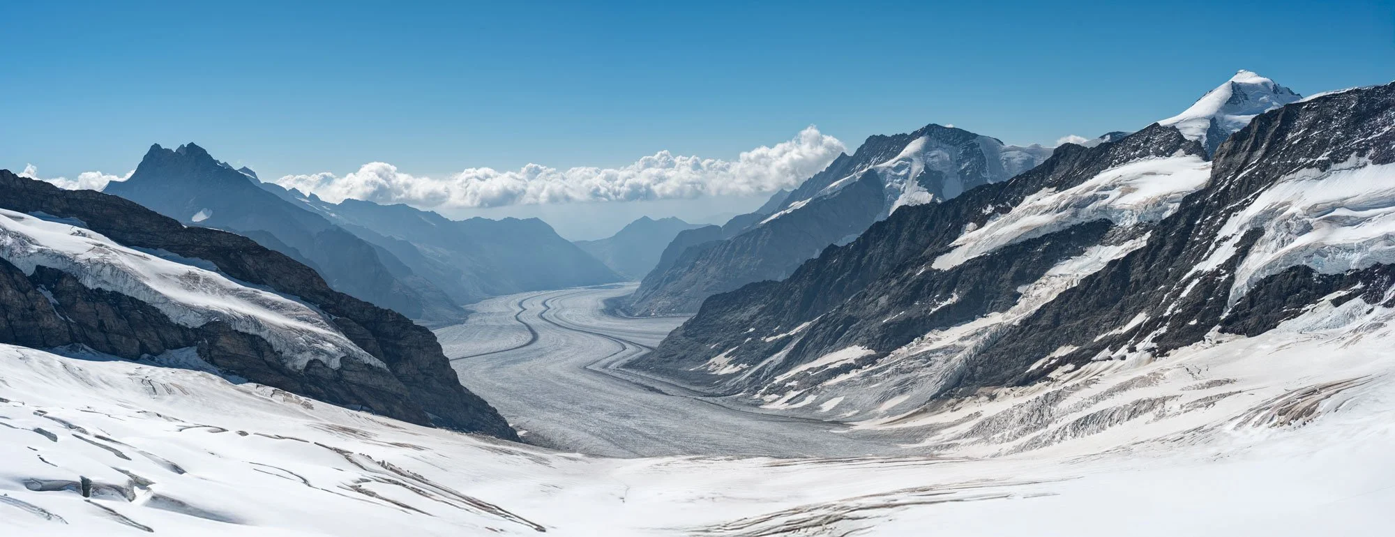 Snow-covered mountain valley with glaciers and mountain peaks under a blue sky with clouds.