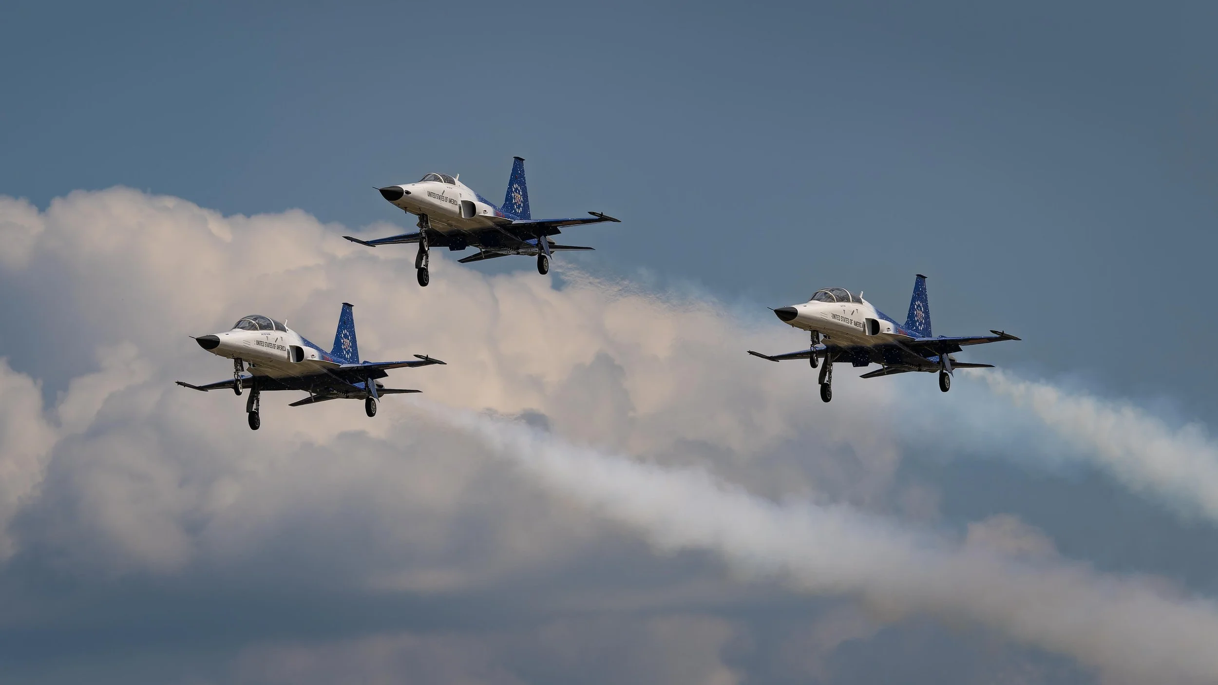 Three blue and white fighter jets flying in formation against a cloudy sky.