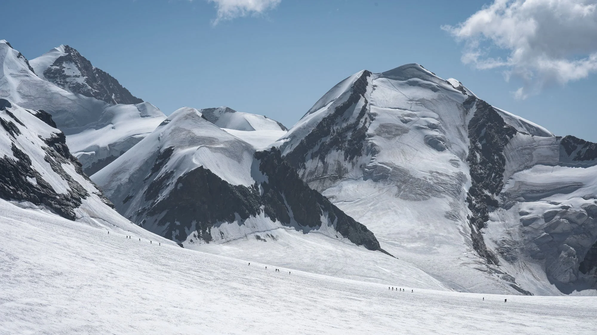 Snow-covered mountain range with large glaciers and a group of climbers in the foreground