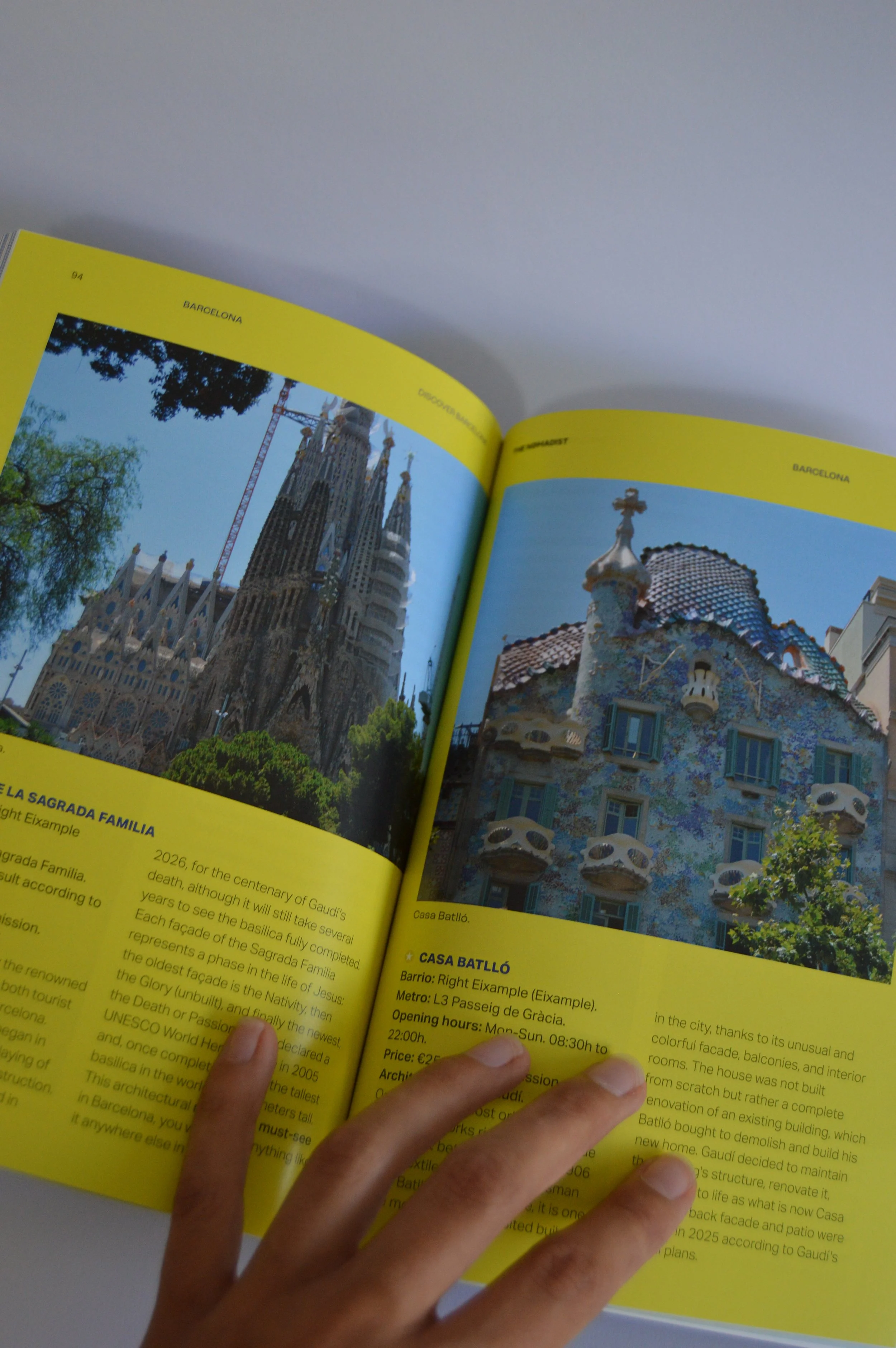 Página amarilla de la guía impresa de Barcelona de The Nomadist, donde aparece información sobre la Sagrada Familia y la Casa Batlló. Una mano sujeta el papel.