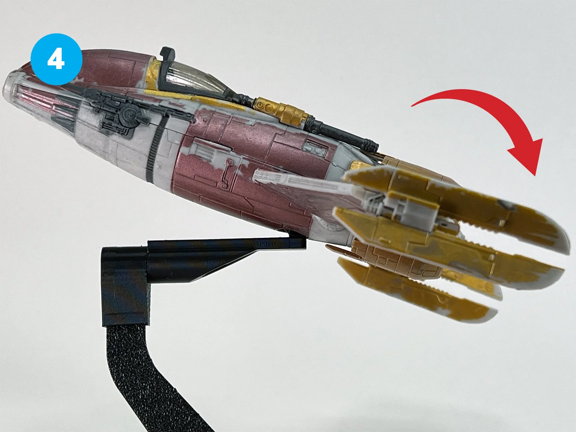 A model spaceship with a yellow wing and red and gray body, mounted on a black stand, with a red arrow indicating upward movement.