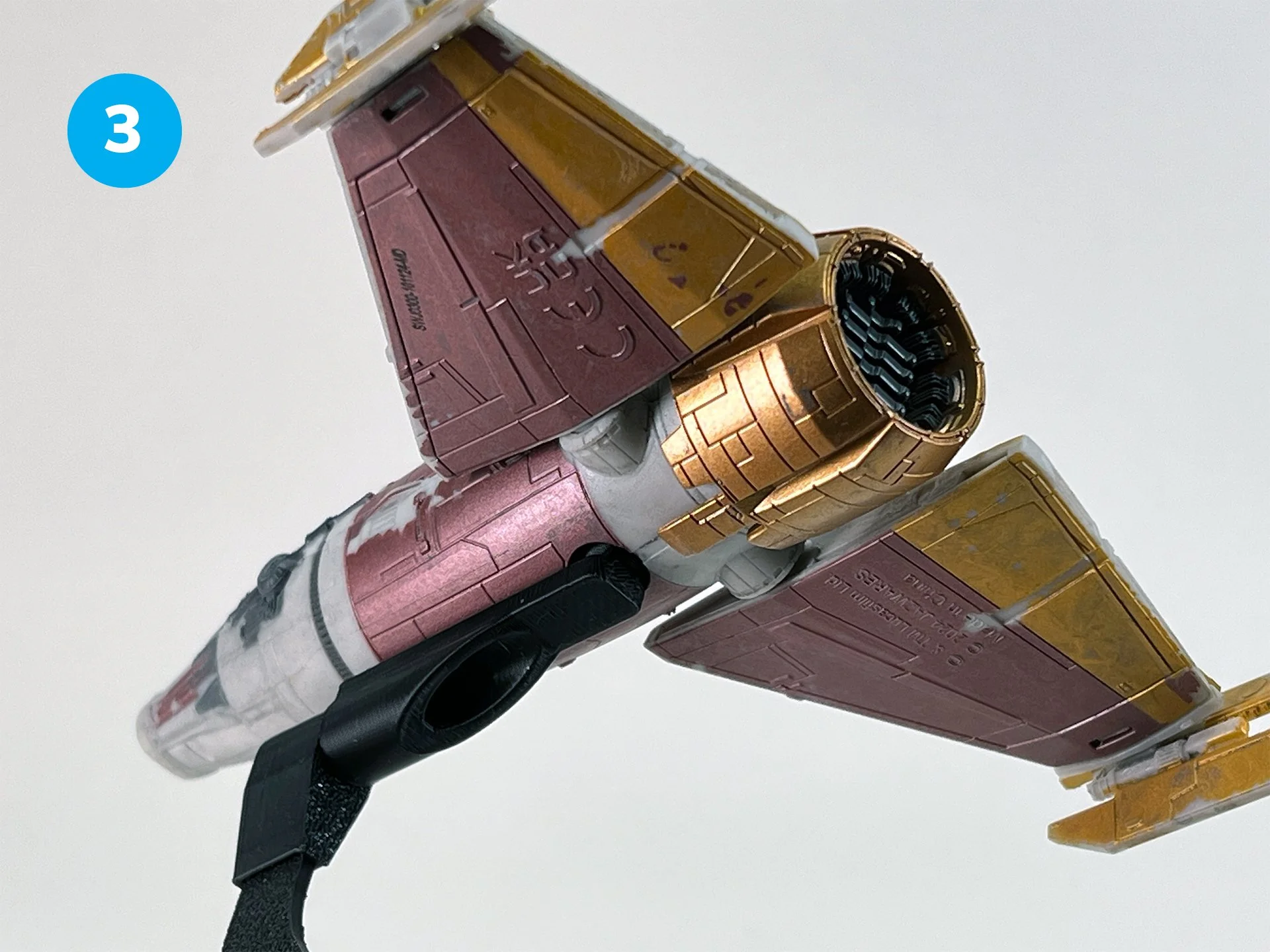 Close-up of a detailed model of an airplane, primarily in pink, white, and gold colors, with a black strap attached.