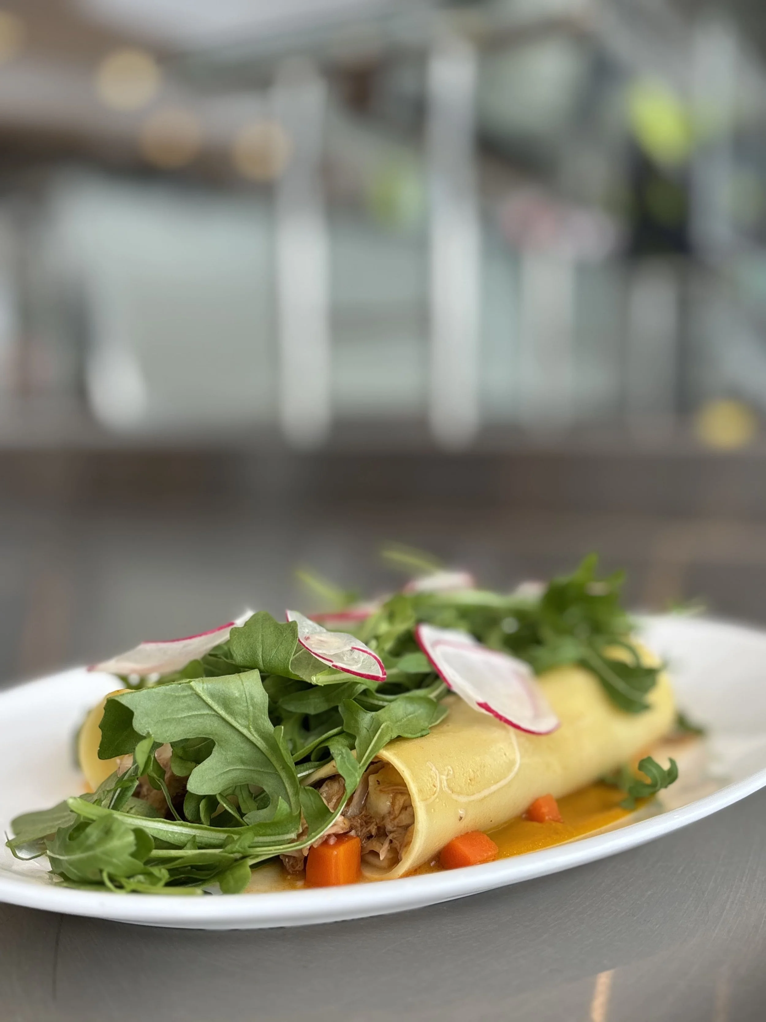 Rouleau de tortilla rempli de légumes verts, radis et carottes, présenté sur une assiette blanche.