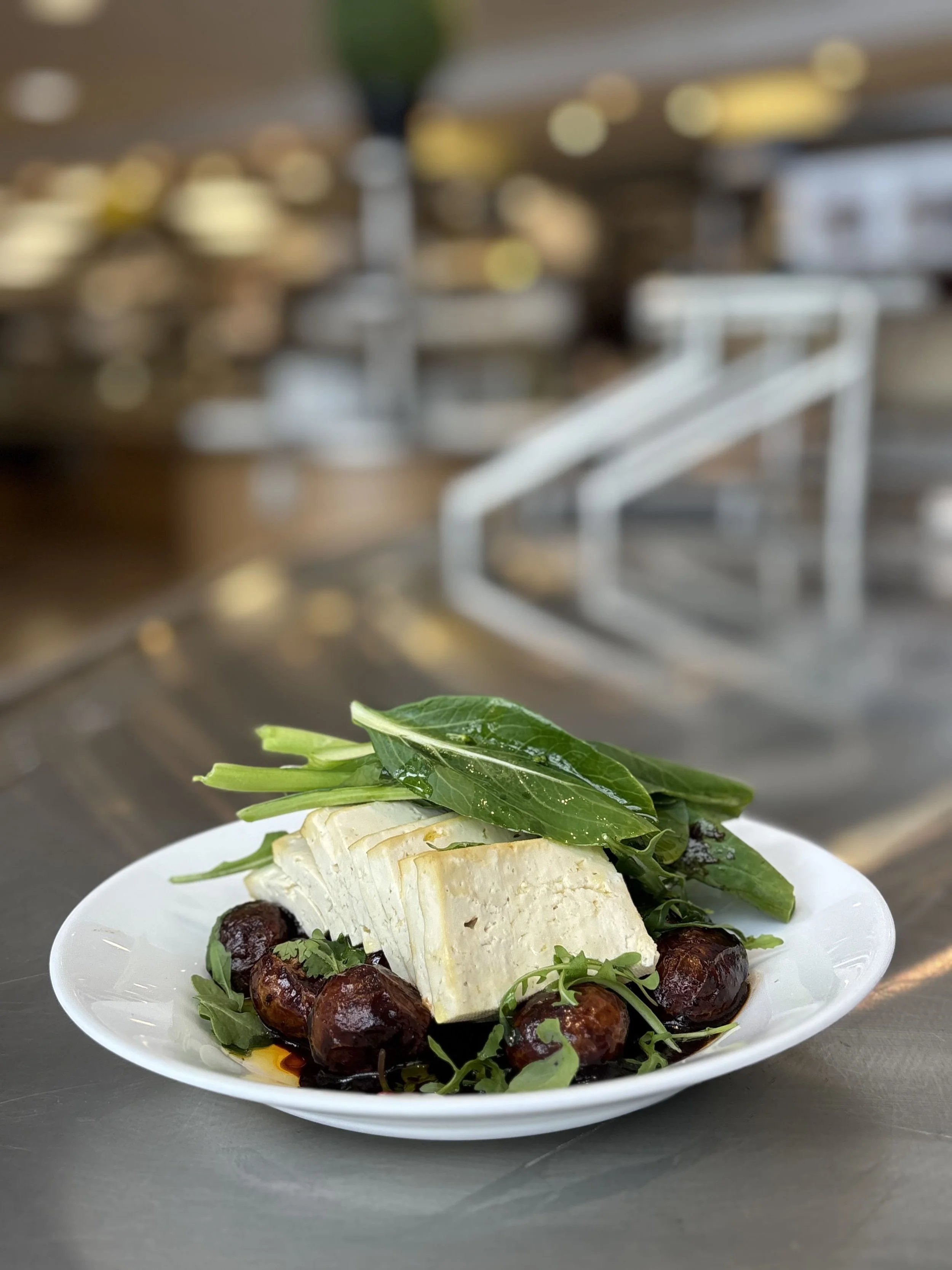 Plat de fromage avec feuilles vertes, olives noires, et une sauce, présenté sur une assiette blanche.