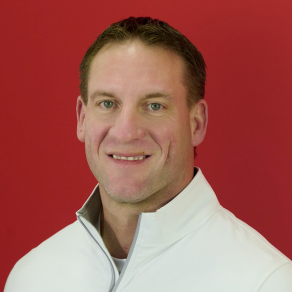 Headshot of a man with short dark hair, wearing a white zip-up jacket, standing against a red background.