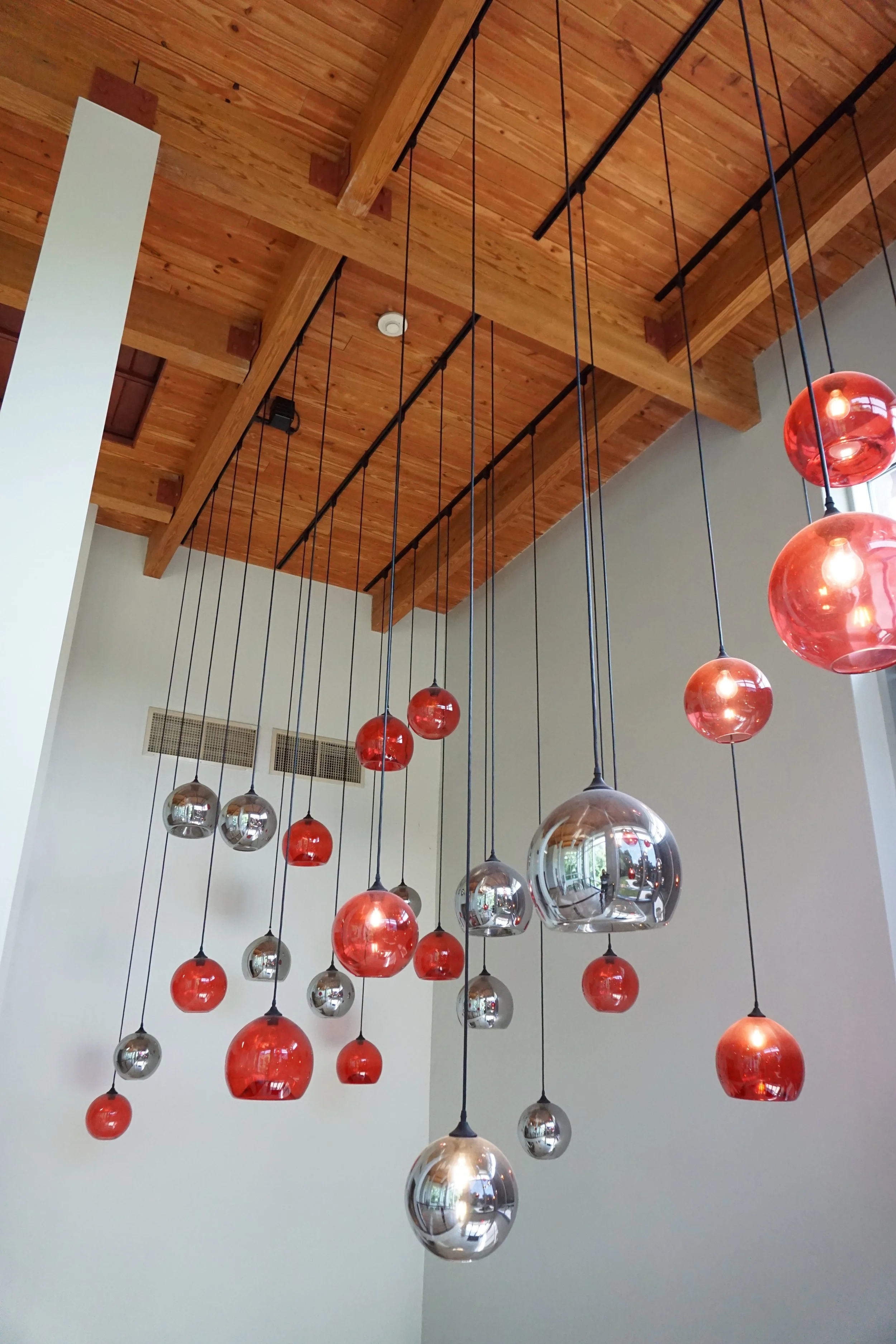 Modern chandelier with multiple hanging glass orbs in red and silver colors in a room with wooden ceiling.