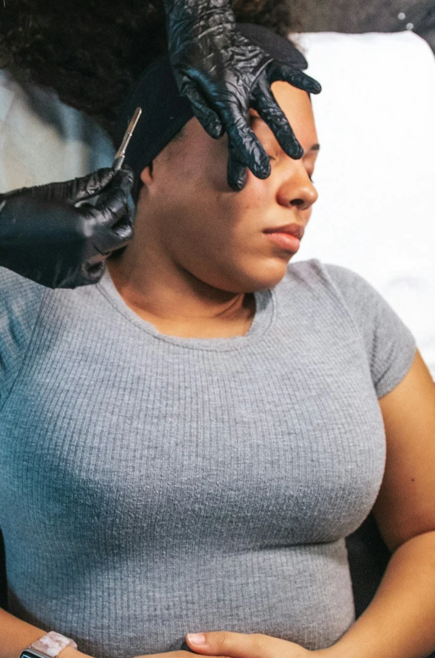 A woman in a gray shirt receiving a cosmetic injection in her forehead.