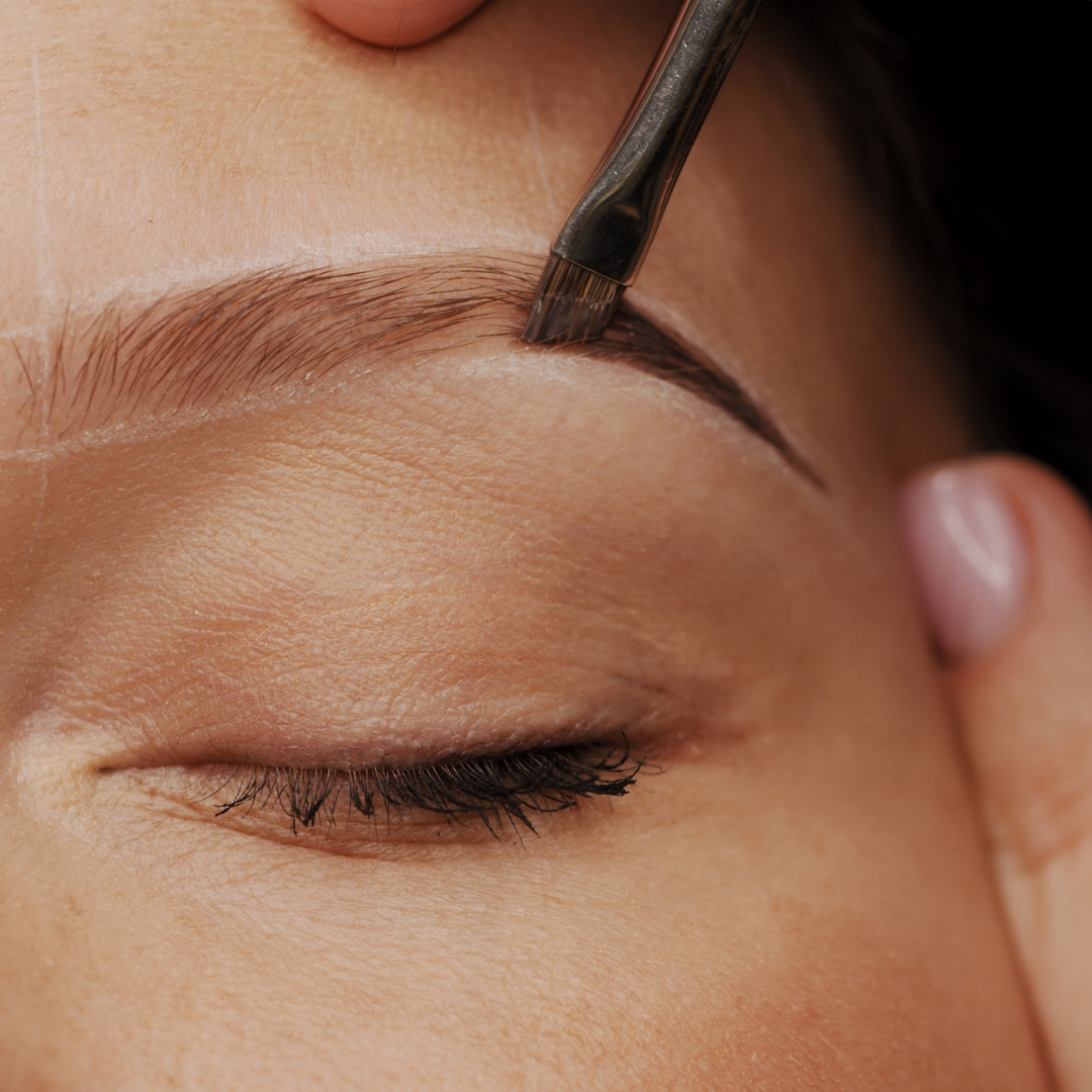 Close-up of a person’s eye with makeup brush applying eyebrow stain.