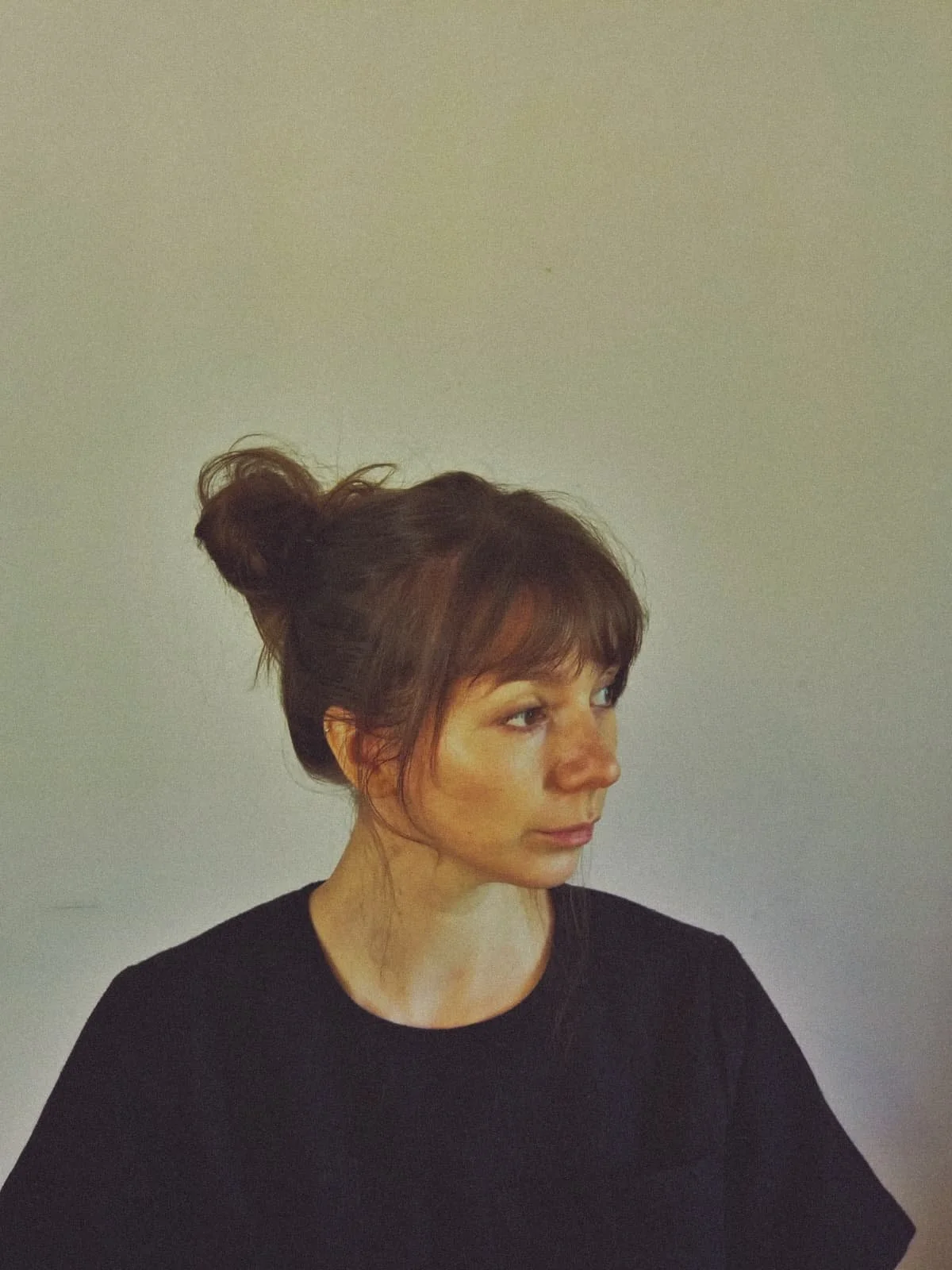 Portrait d'une femme aux cheveux bruns en chignon, portant un haut noir, regardant vers la droite, avec un fond gris clair.