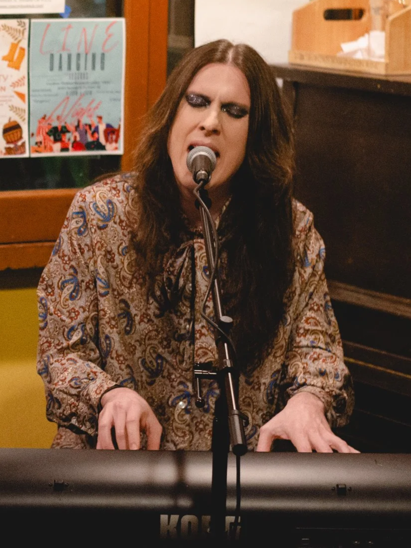 A straight-on image of Cody Riker singing and playing keyboard.