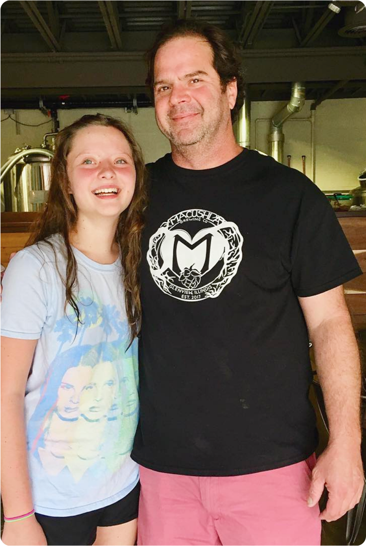 A man and a girl smiling and standing together in an indoor setting, possibly a brewery or similar venue.