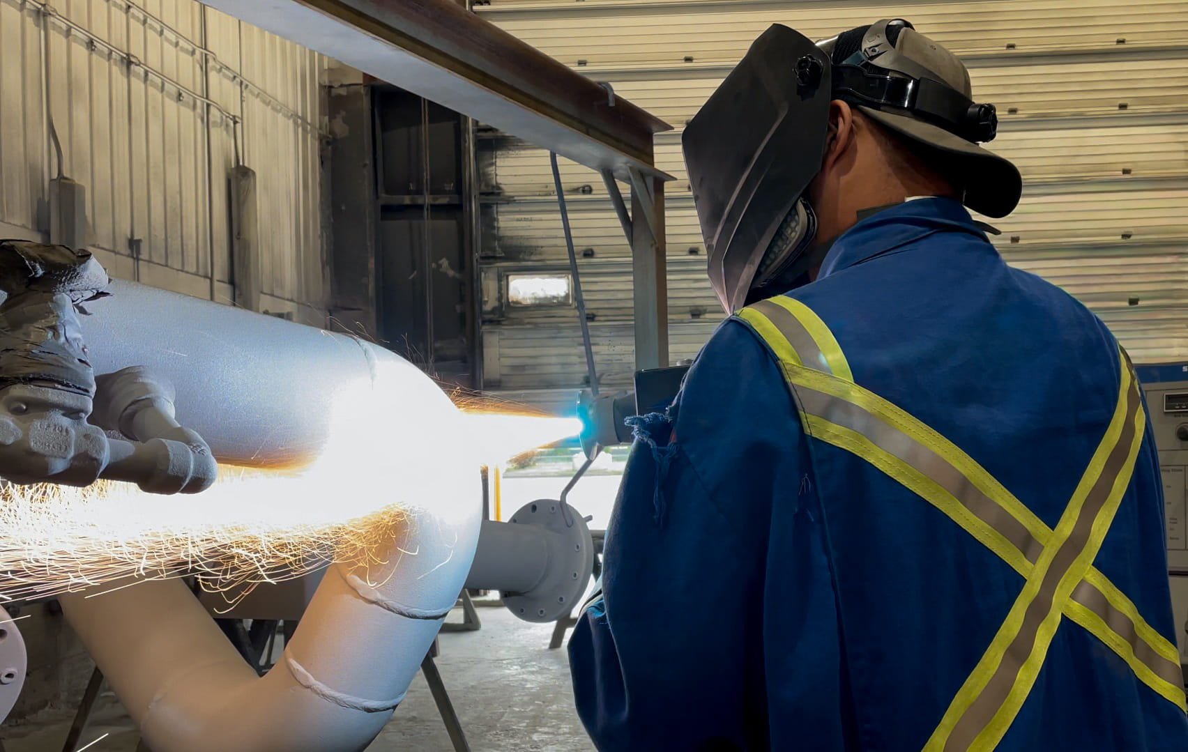 A worker in a blue safety jacket and coating a oilfield pipe with thermal/ combustion spray in Alberta, Canada.