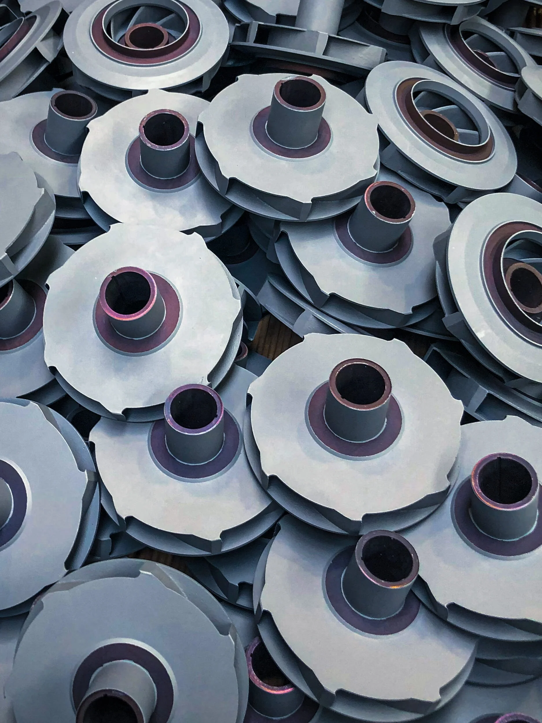 A large pile of metallic mechanical components, possibly gears or pulleys, with a central cylindrical hole, stacked together.