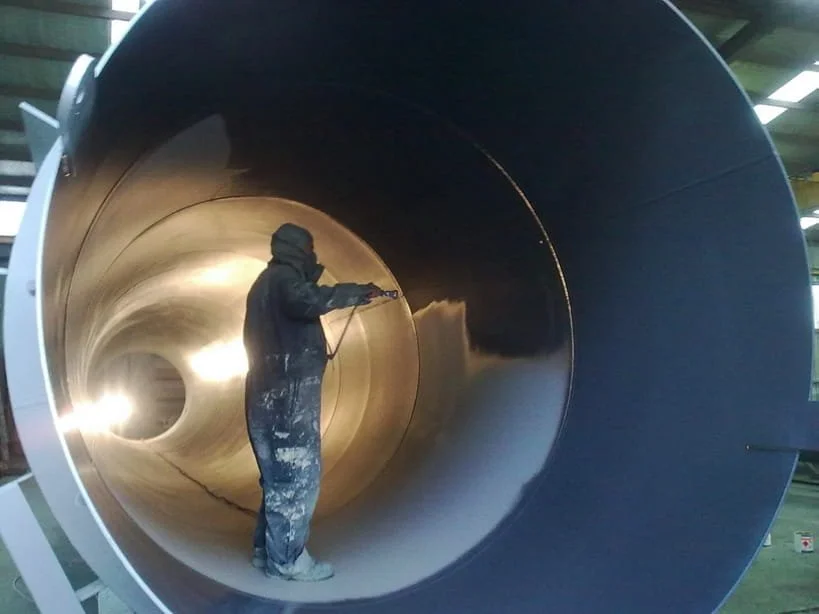 A worker painting an internal pipe lining on the inside of a large industrial pipe in Edmonton, Alberta.