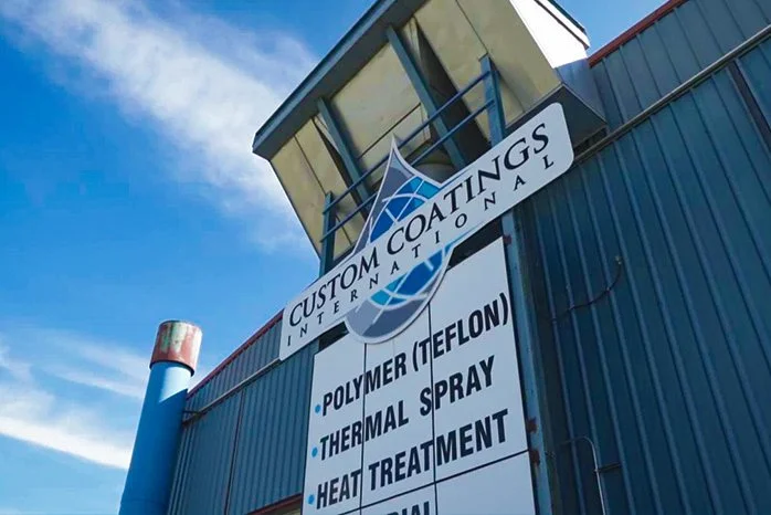 Custom Coatings International Shop Photo from the outside, showing a sign featuring sandblasting and protective coating services on a sign