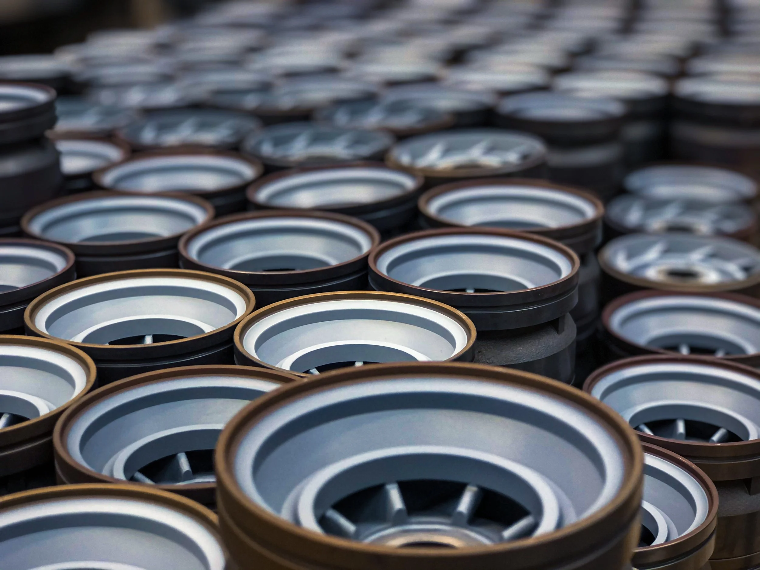A close-up view of multiple Teflon coated downhole components for oil and gas arranged in rows, with some stacked on top of each other, outdoors.