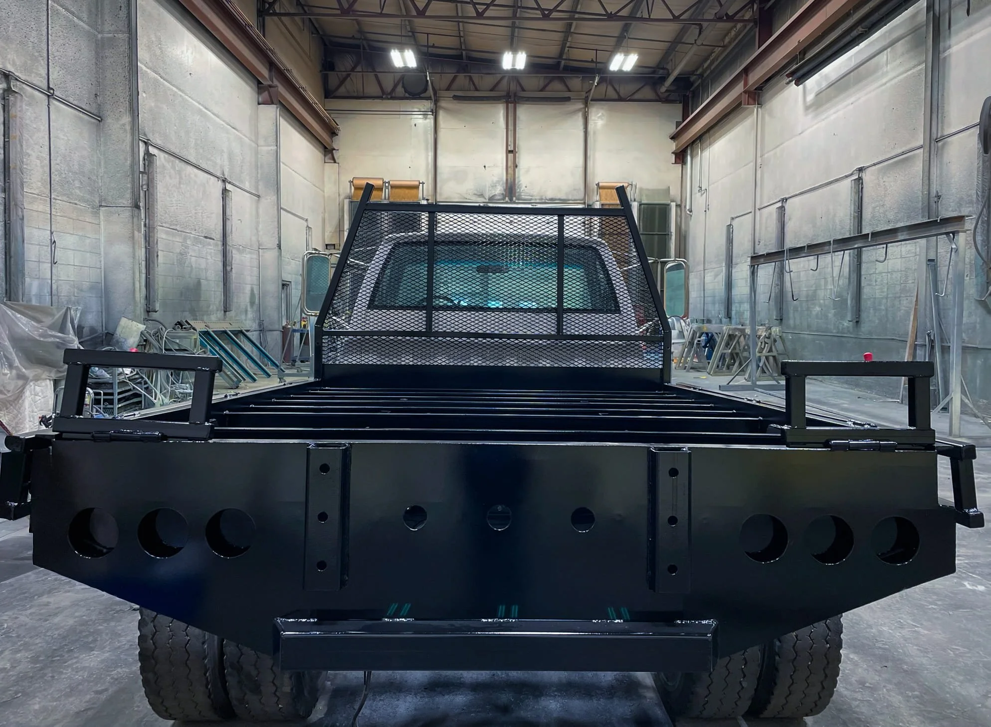 A black utility flatbed truck inside an industrial workshop showcasing powder coating services