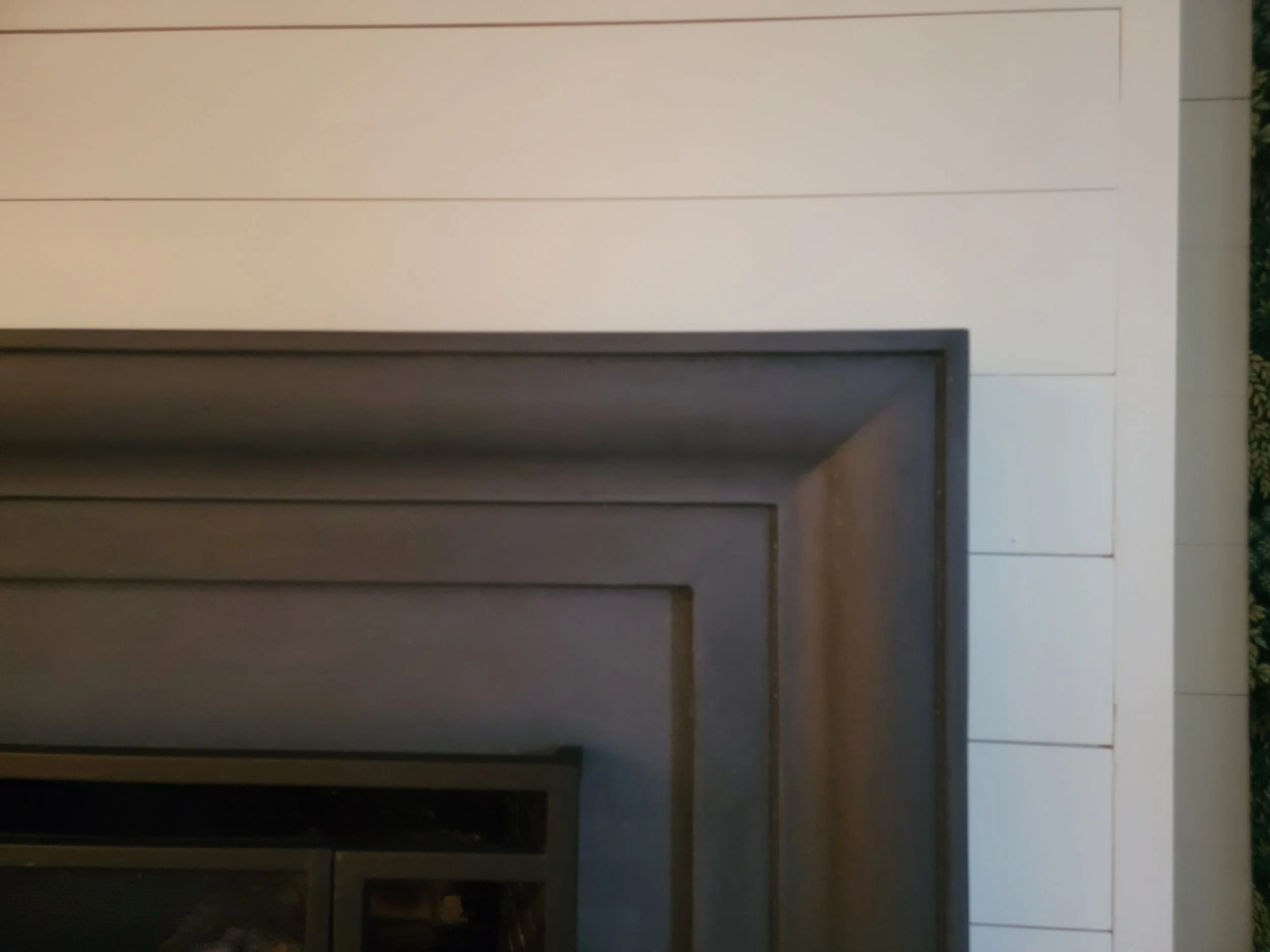 Close-up of a section of an indoor fireplace with dark brown molding, surrounded by white wall panels and beige tile flooring.