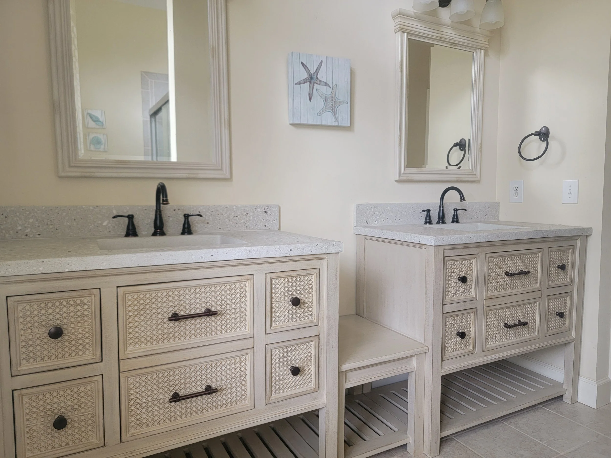 Two bathroom vanities with matching framed mirrors, starfish artwork, and black fixtures in a light-colored bathroom.
