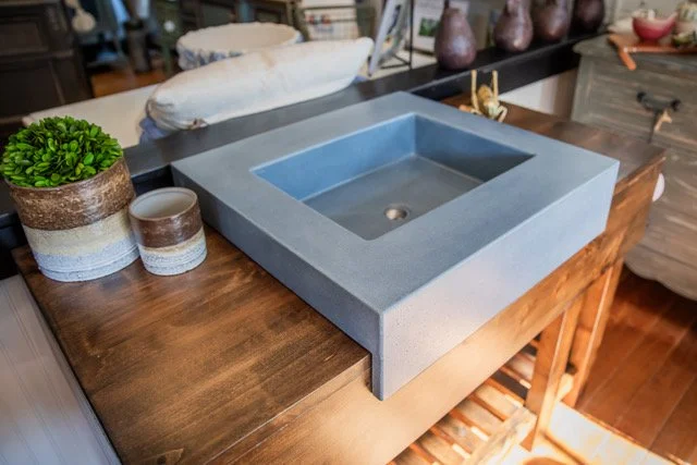 A modern square blue sink with a hole in the center is placed on a wooden countertop, with decorative pottery and a plant nearby.