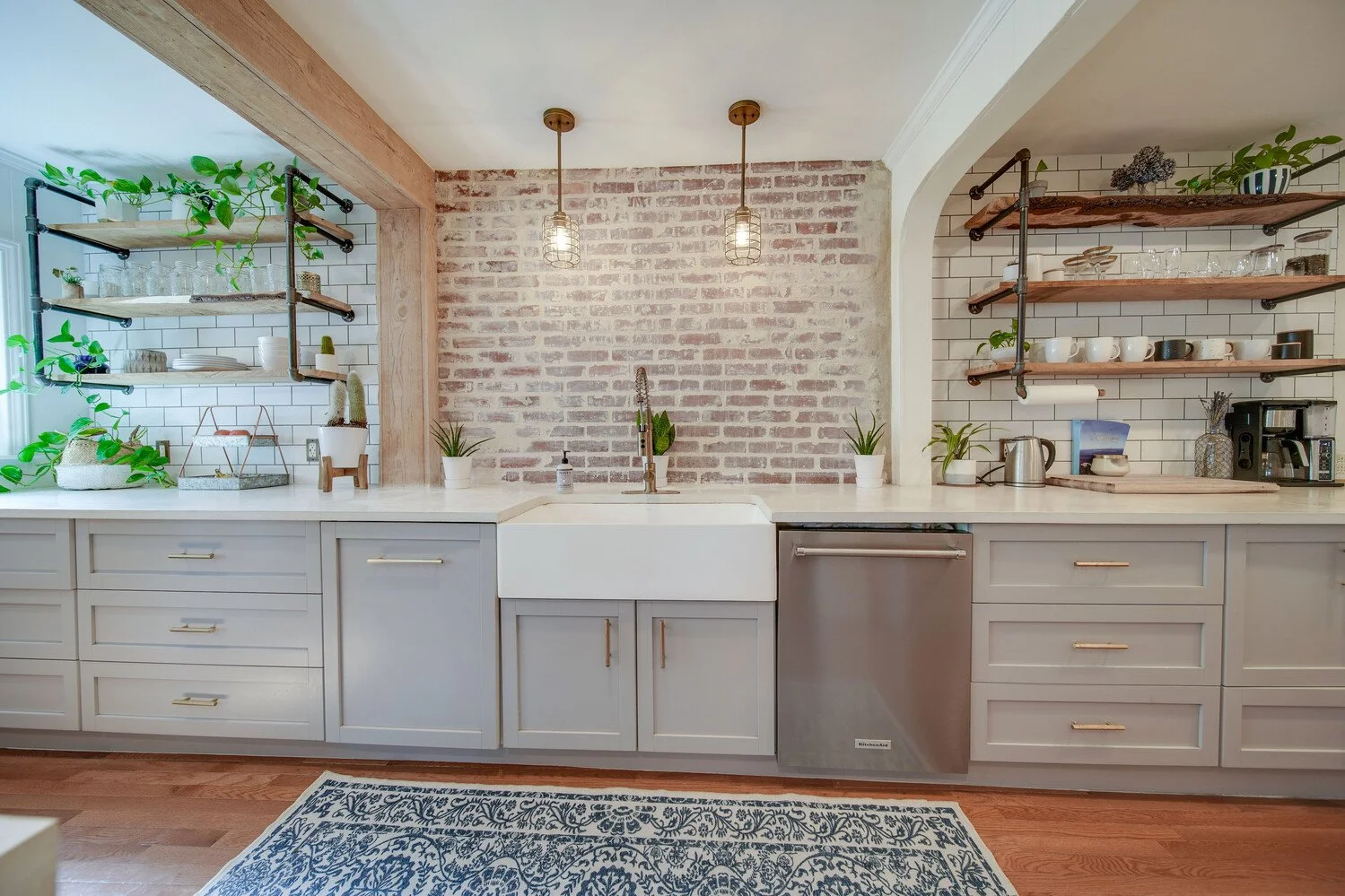 Modern kitchen with white cabinets, brick backsplash, open shelves, potted plants, and a farmhouse sink.