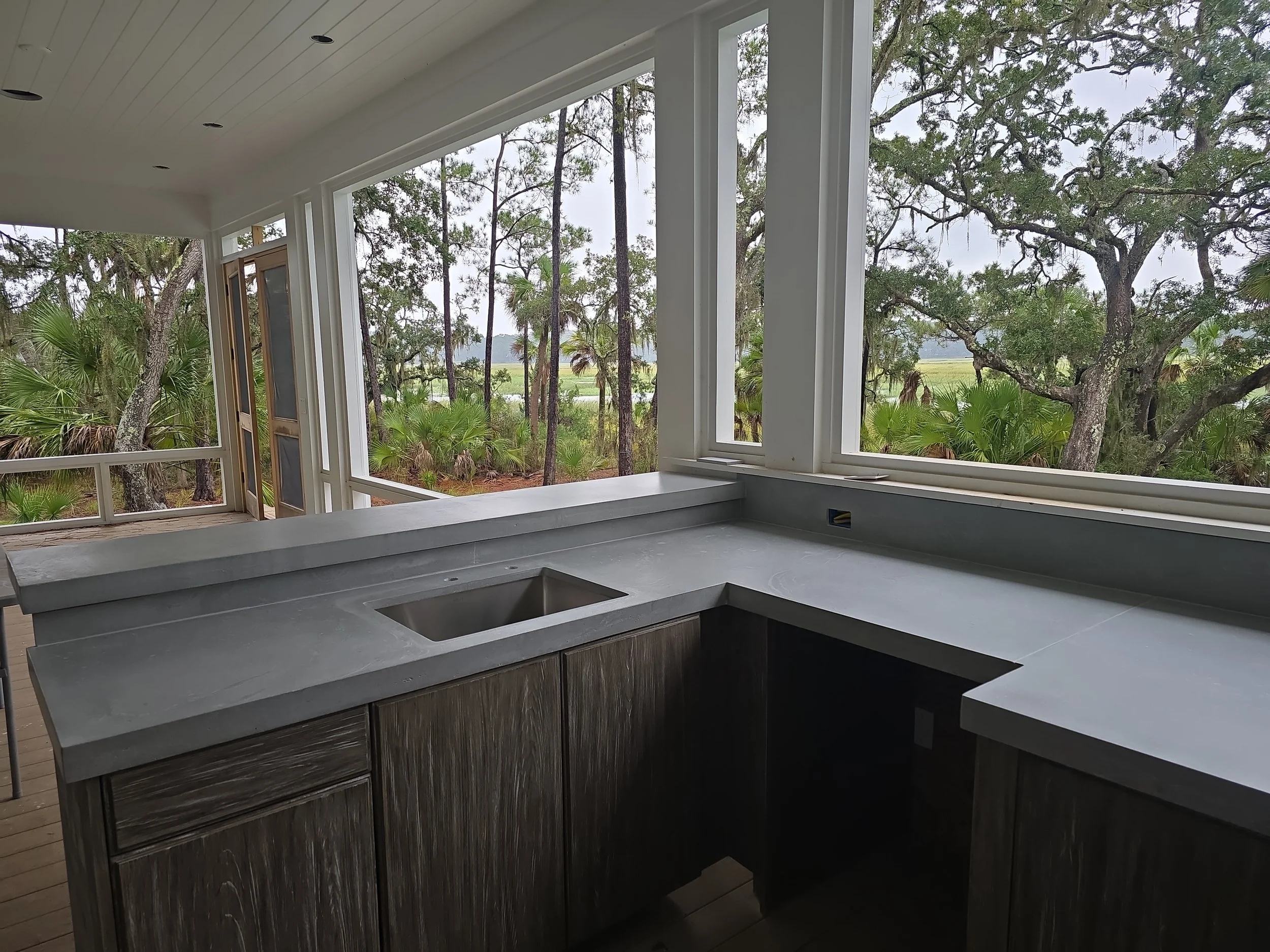 Gray concrete countertop with an integral rectangular sink and matching backsplash in a screened outdoor kitchen