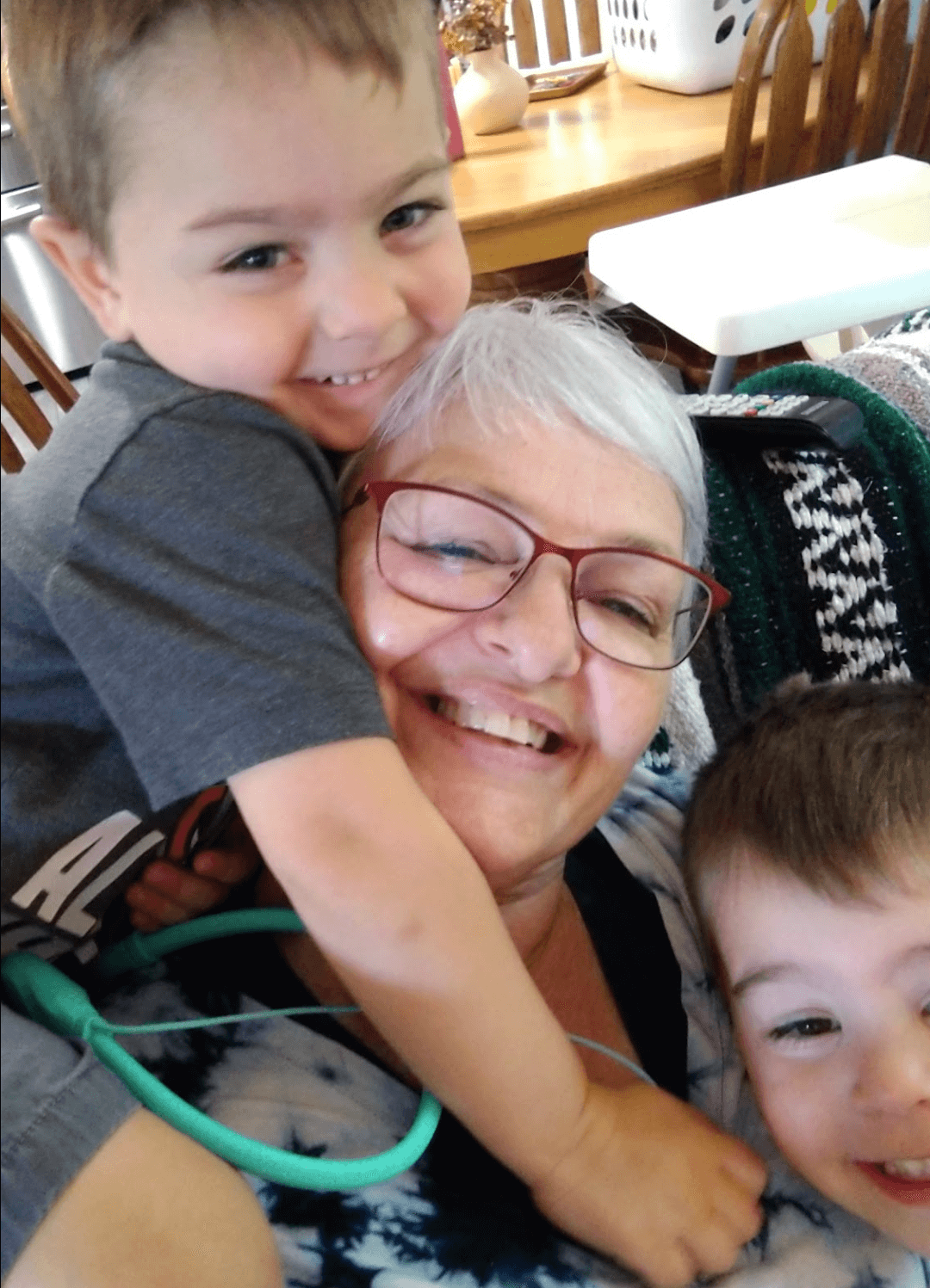 A happy artist, June Lizotte is playing with 2 grandsons, who are giving her hugs and kisses in a cozy home setting.