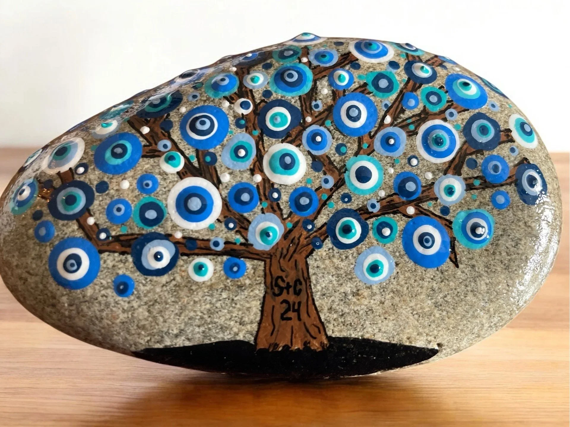 Painted rock with a tree design and blue leaves on its branches includes carved initials on the trunk.